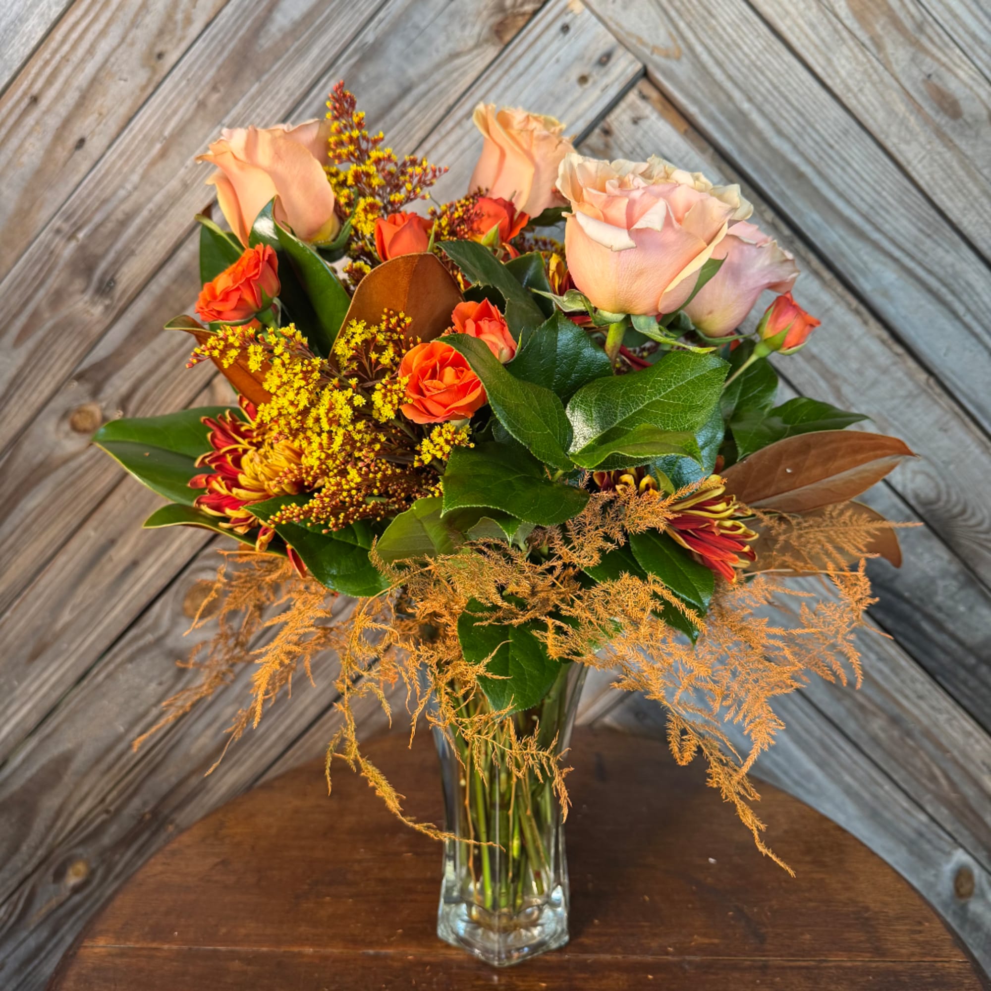Mixed bouquet of peach roses, orange blooms, and yellow filler in a clear vase