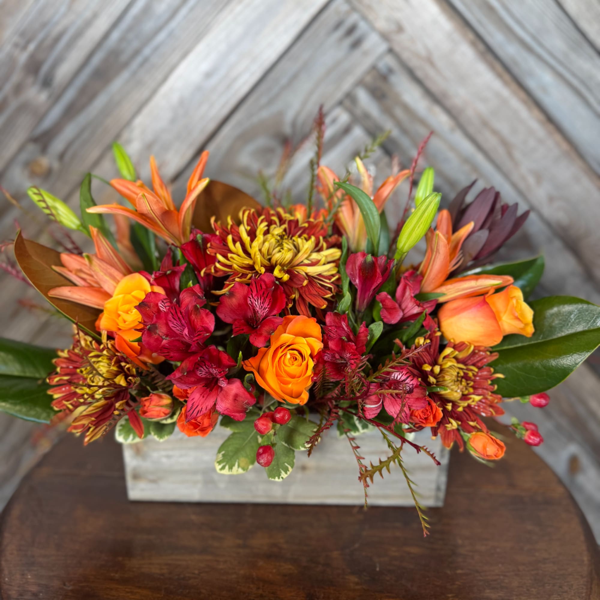 Orange and red mixed flower arrangement in a rustic wooden box