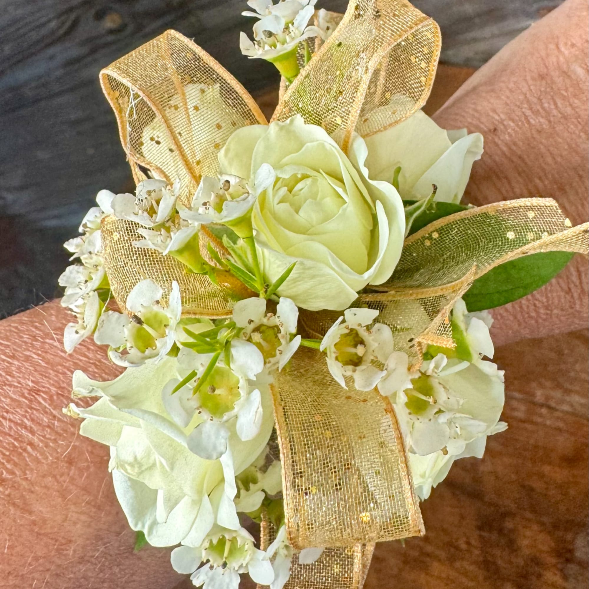 White floral wrist corsage with a gold ribbon bow