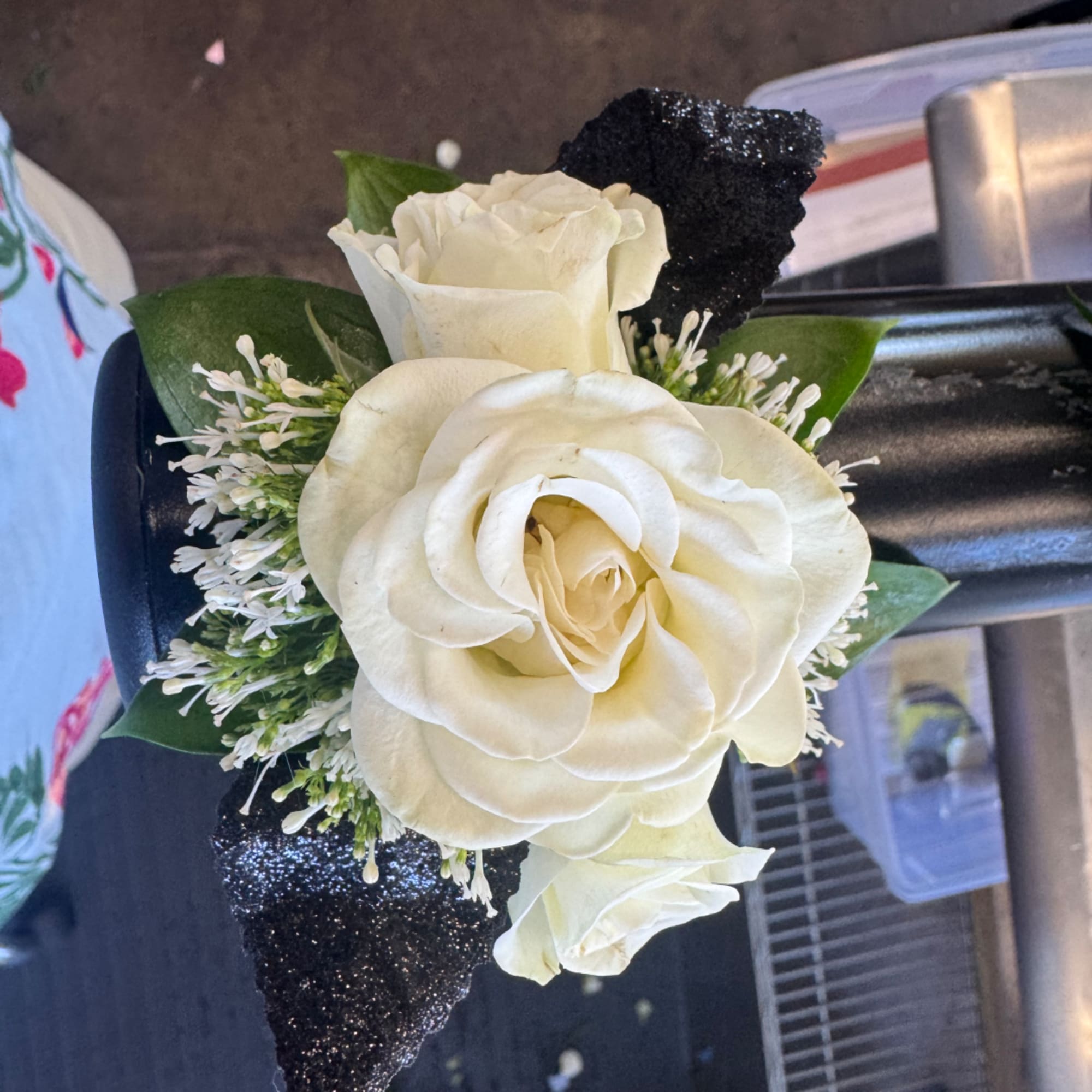 White rose boutonniere with black glitter accents and green leaves