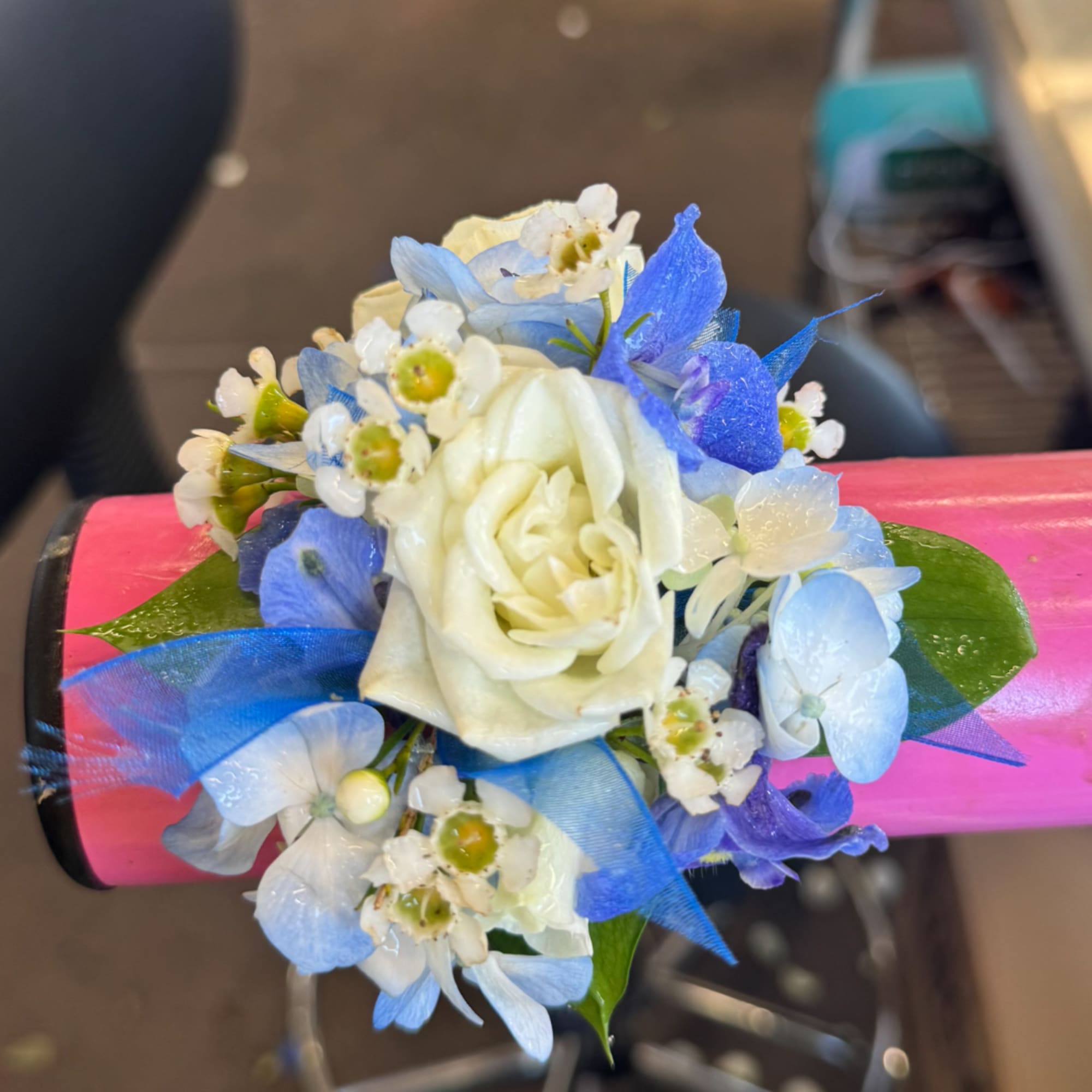 Small blue and white floral corsage with a cream rose on pink wrap
