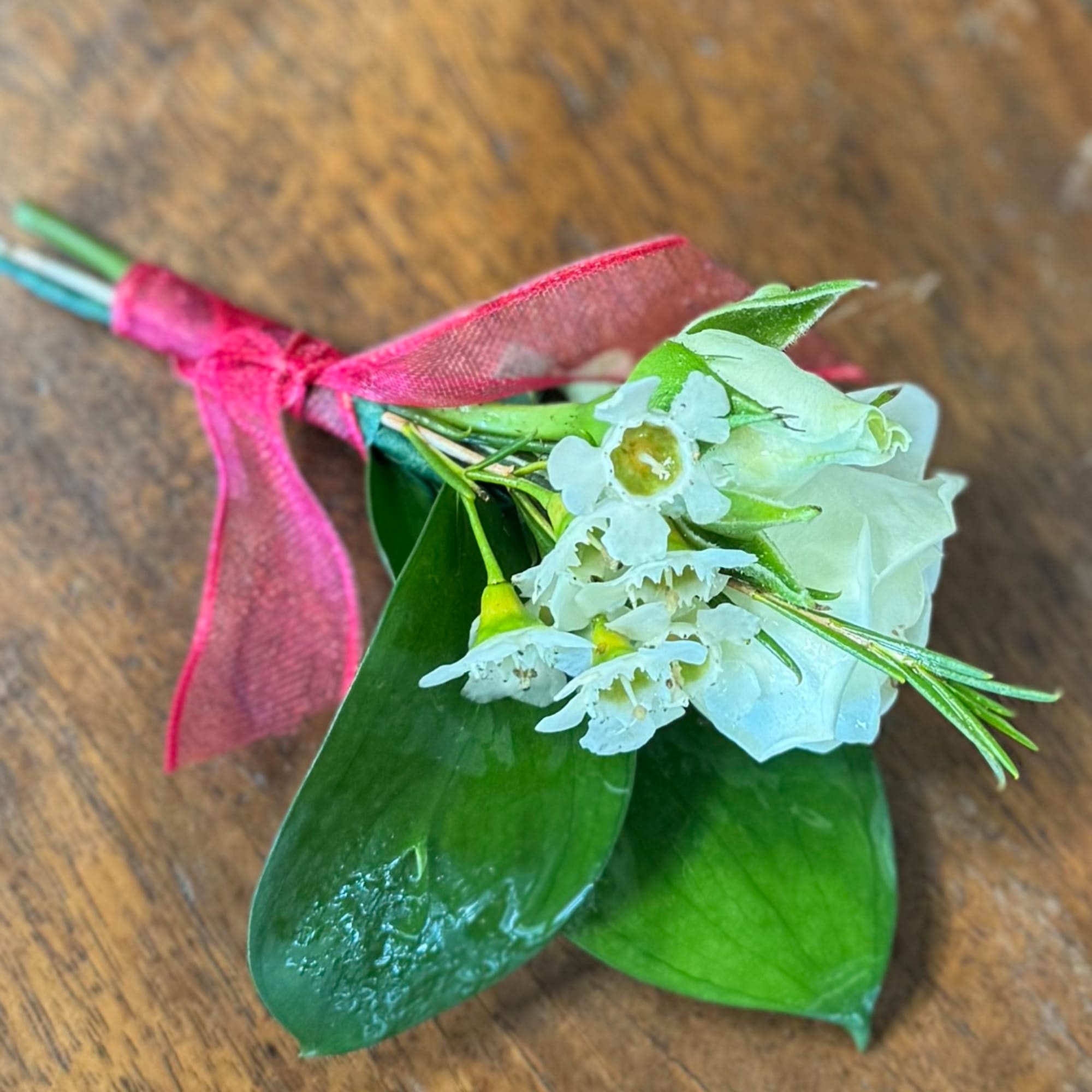 Small white floral boutonniere with pink ribbon on a wooden surface