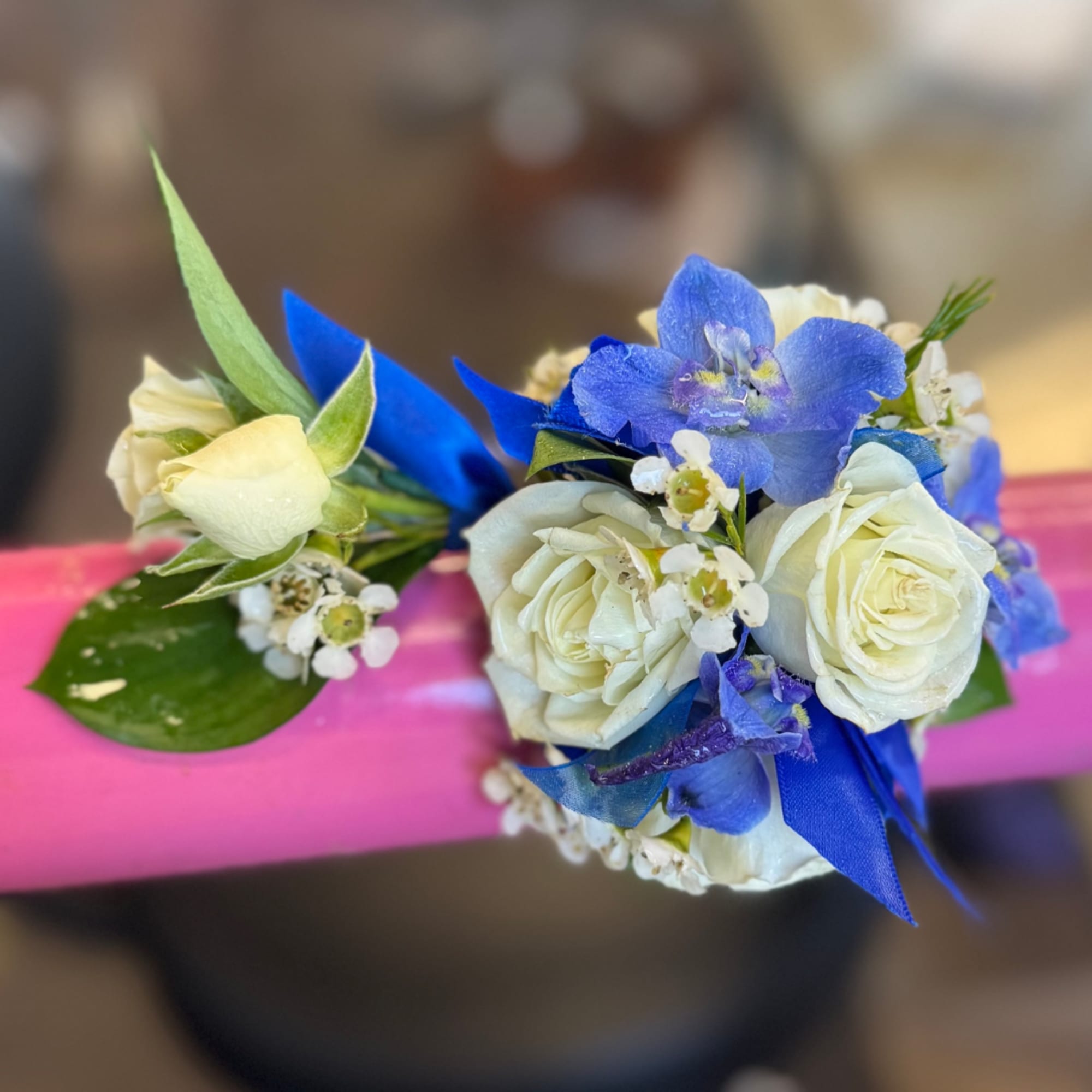 White and blue floral wrist corsage with ribbon on a pink band