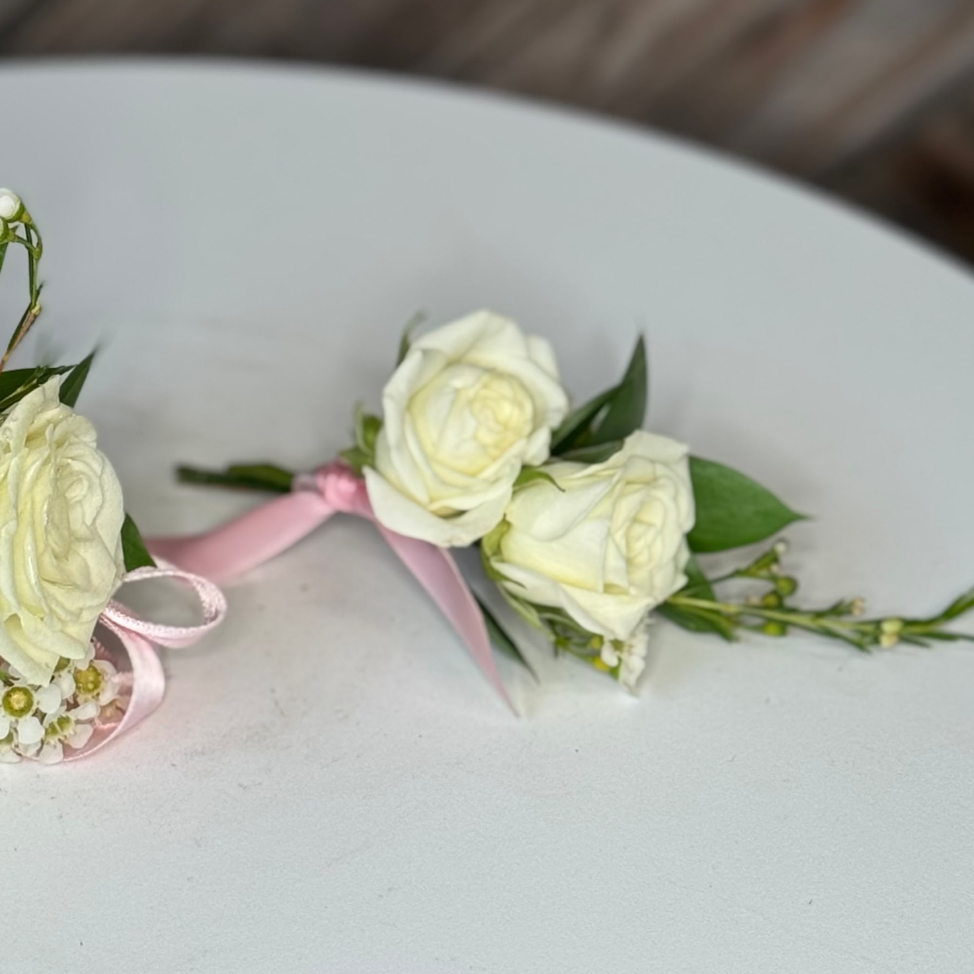 White rose boutonniere with pink ribbon on a white surface