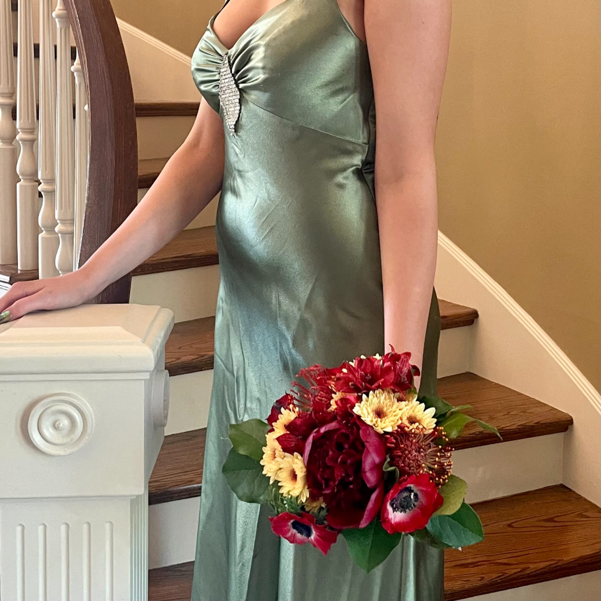 Woman in a satin dress holding a red and yellow bouquet on a staircase