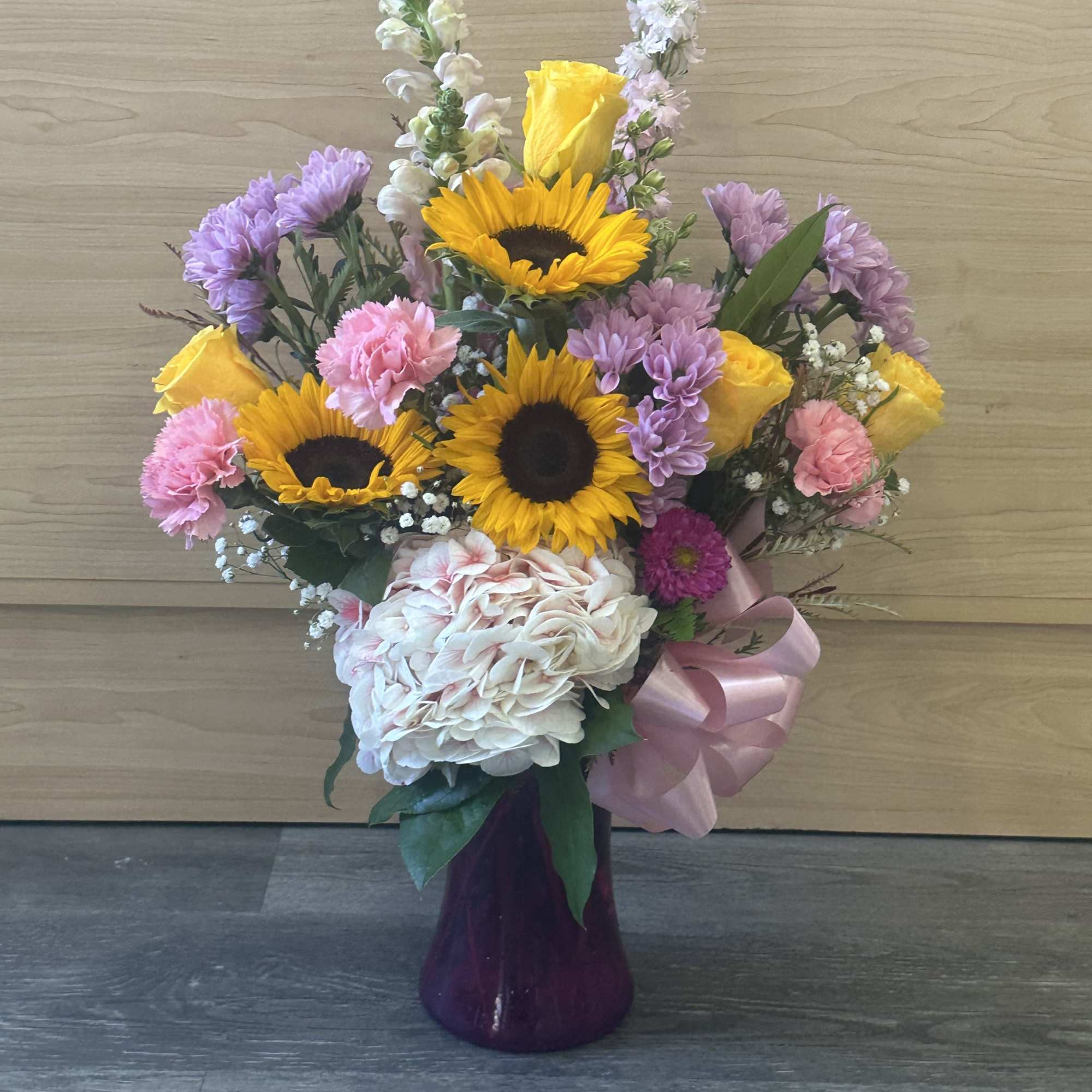 Mixed bouquet with sunflowers, roses, hydrangea, and carnations in a purple vase