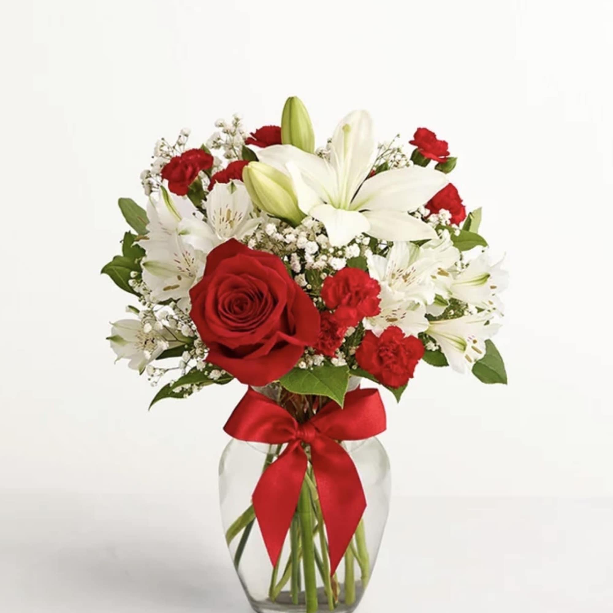 Red roses and white lilies arranged in a glass vase with a red ribbon