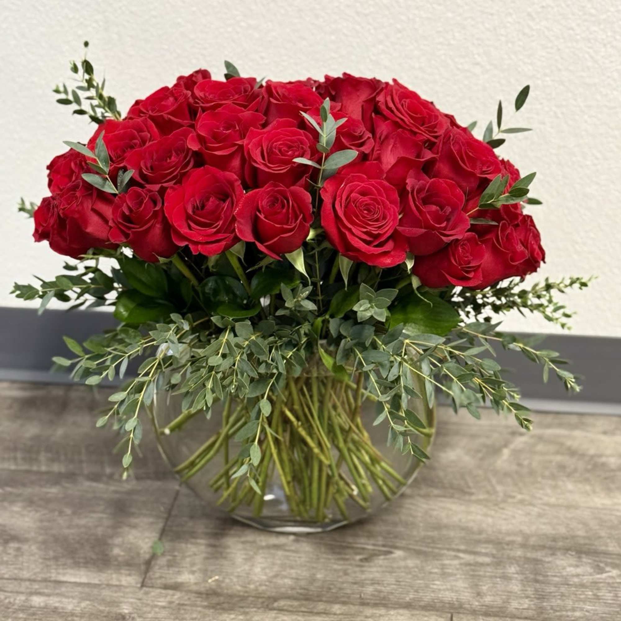 Red roses arranged in a clear glass vase with greenery