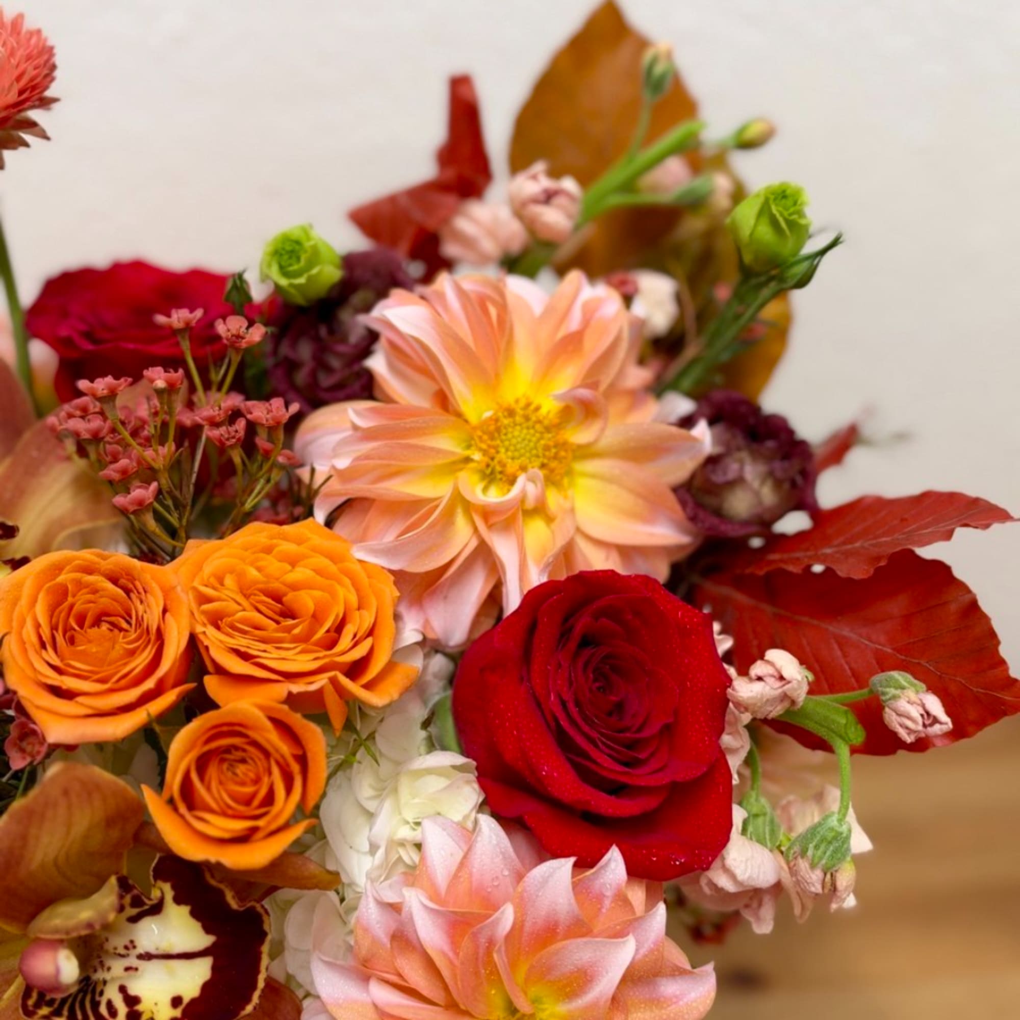 Bouquet of orange, red, and blush flowers with autumn leaves