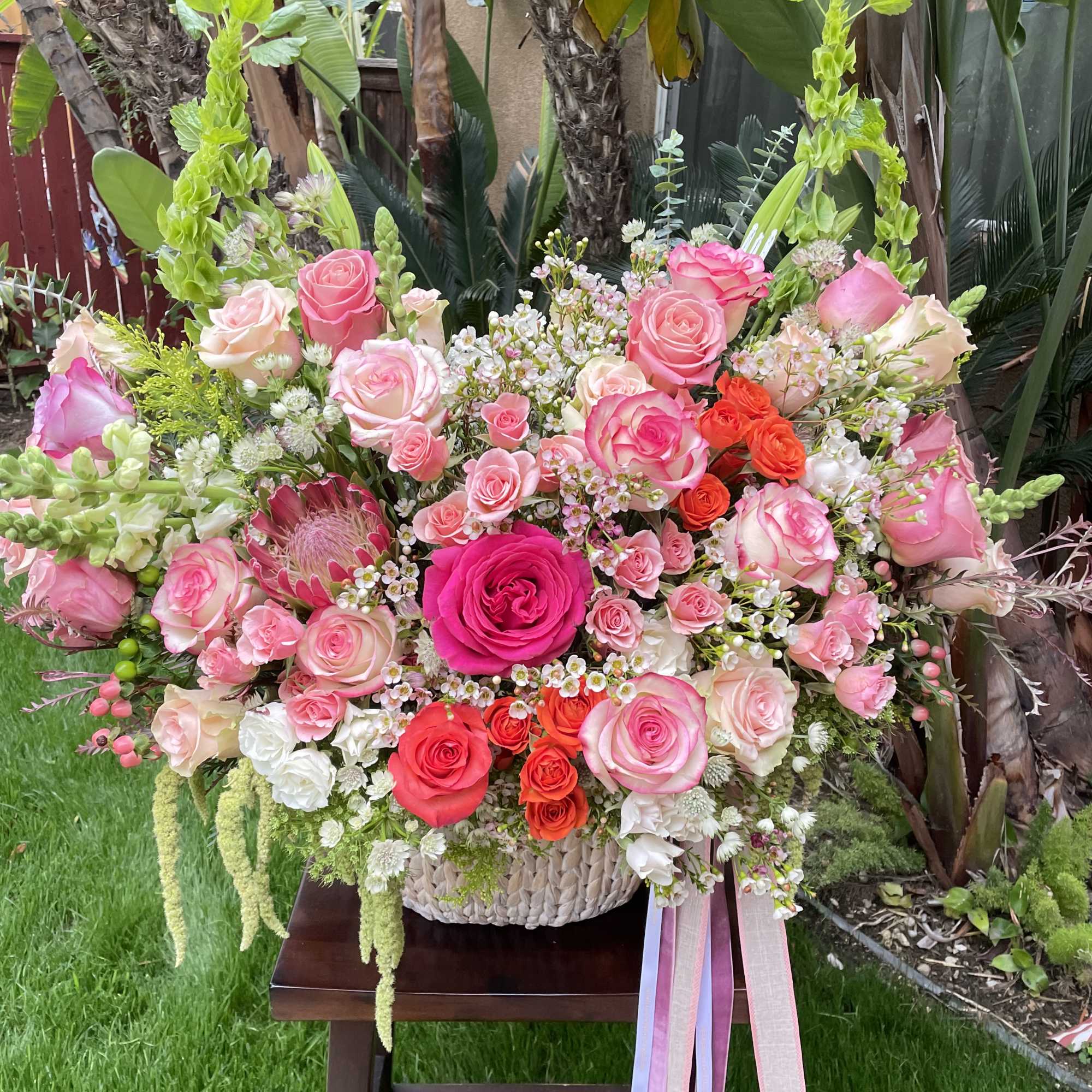Large basket arrangement of pink and coral roses with ribbon tails