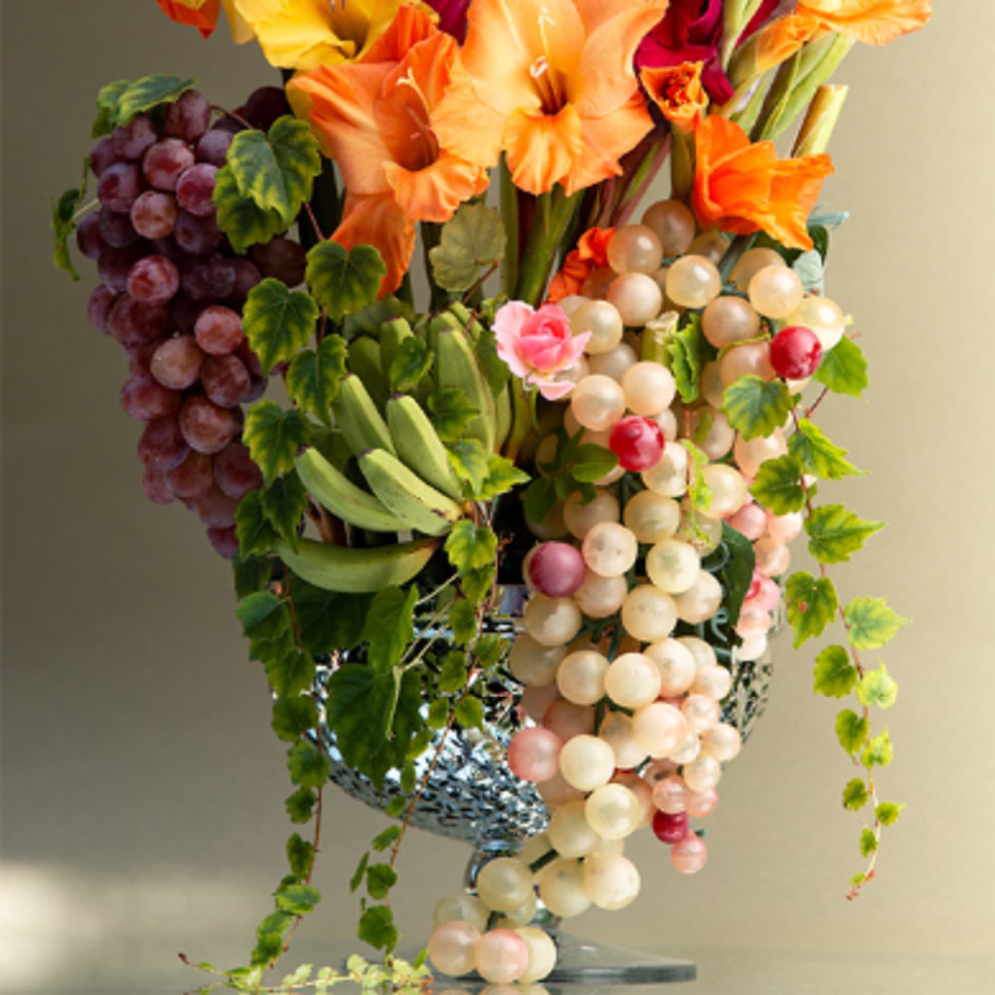 Arrangement of orange flowers with clusters of grapes in a silver vase