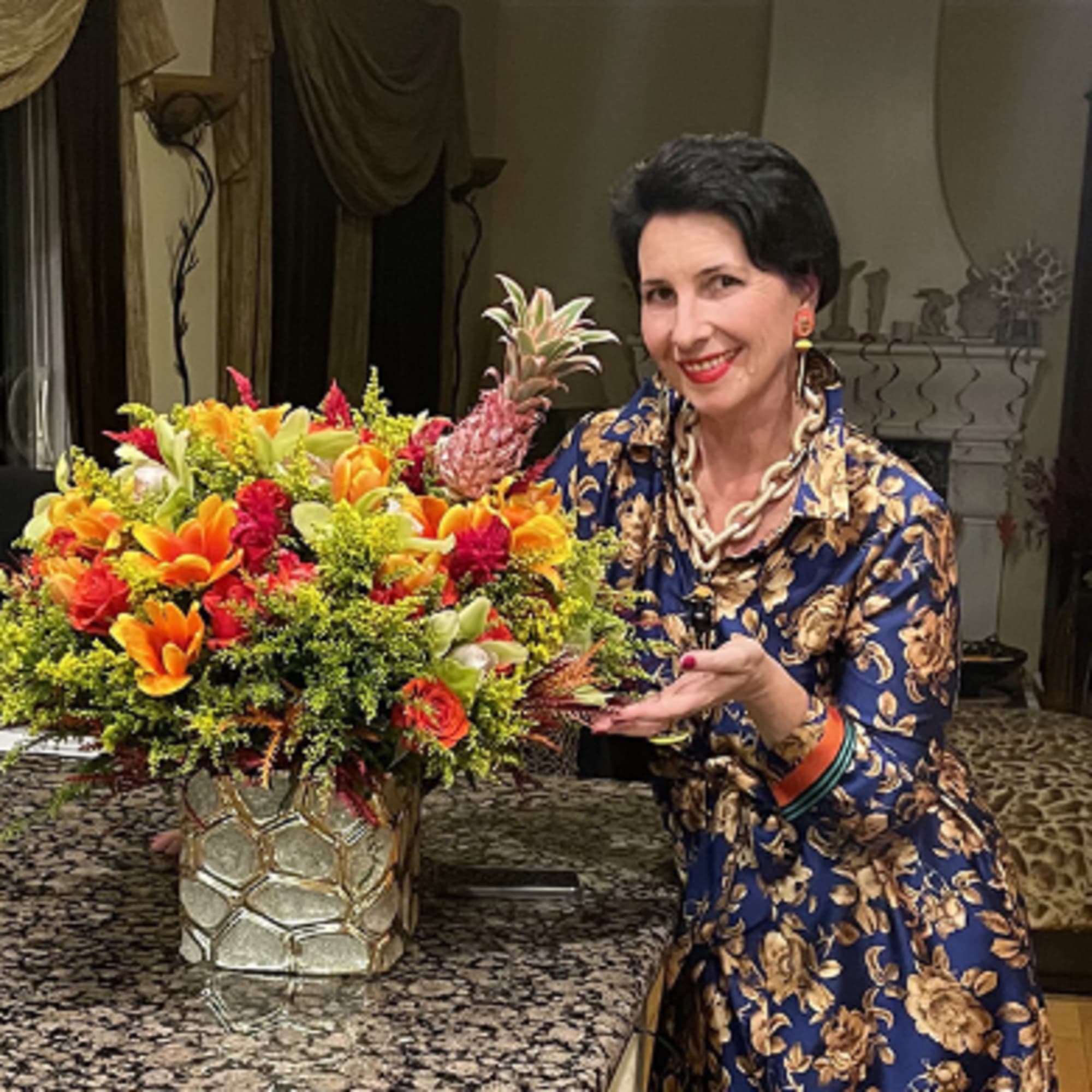 Woman posing beside a large colorful floral arrangement in a metallic vase