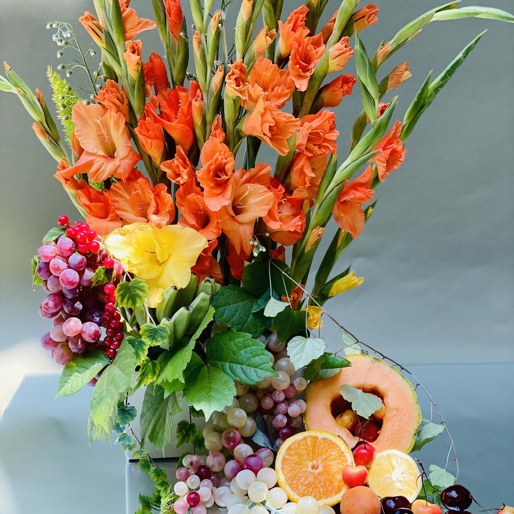 Tall orange floral arrangement with grapes and sliced fruit in a vase
