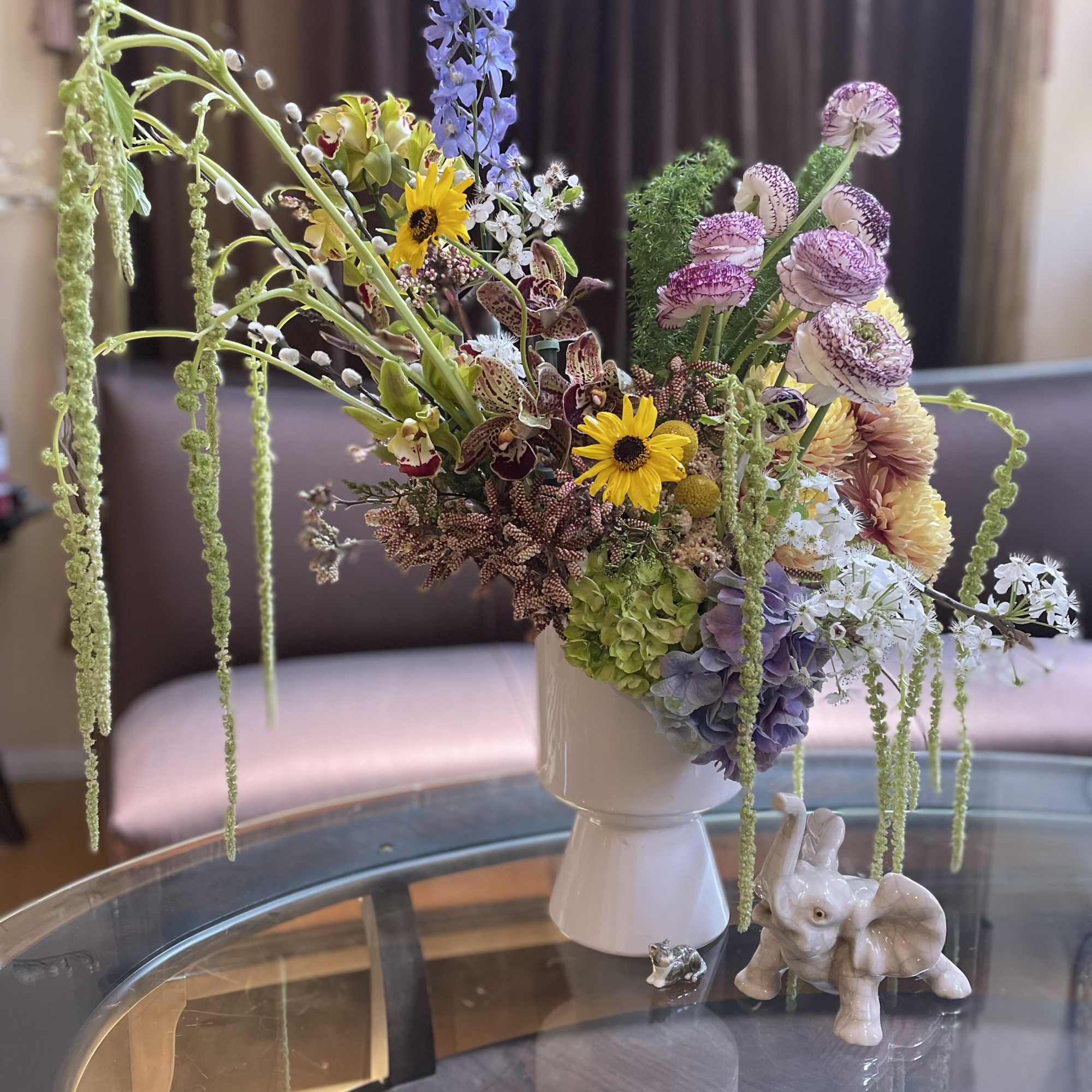 Mixed bouquet in a white vase with trailing blooms and a small elephant figurine nearby