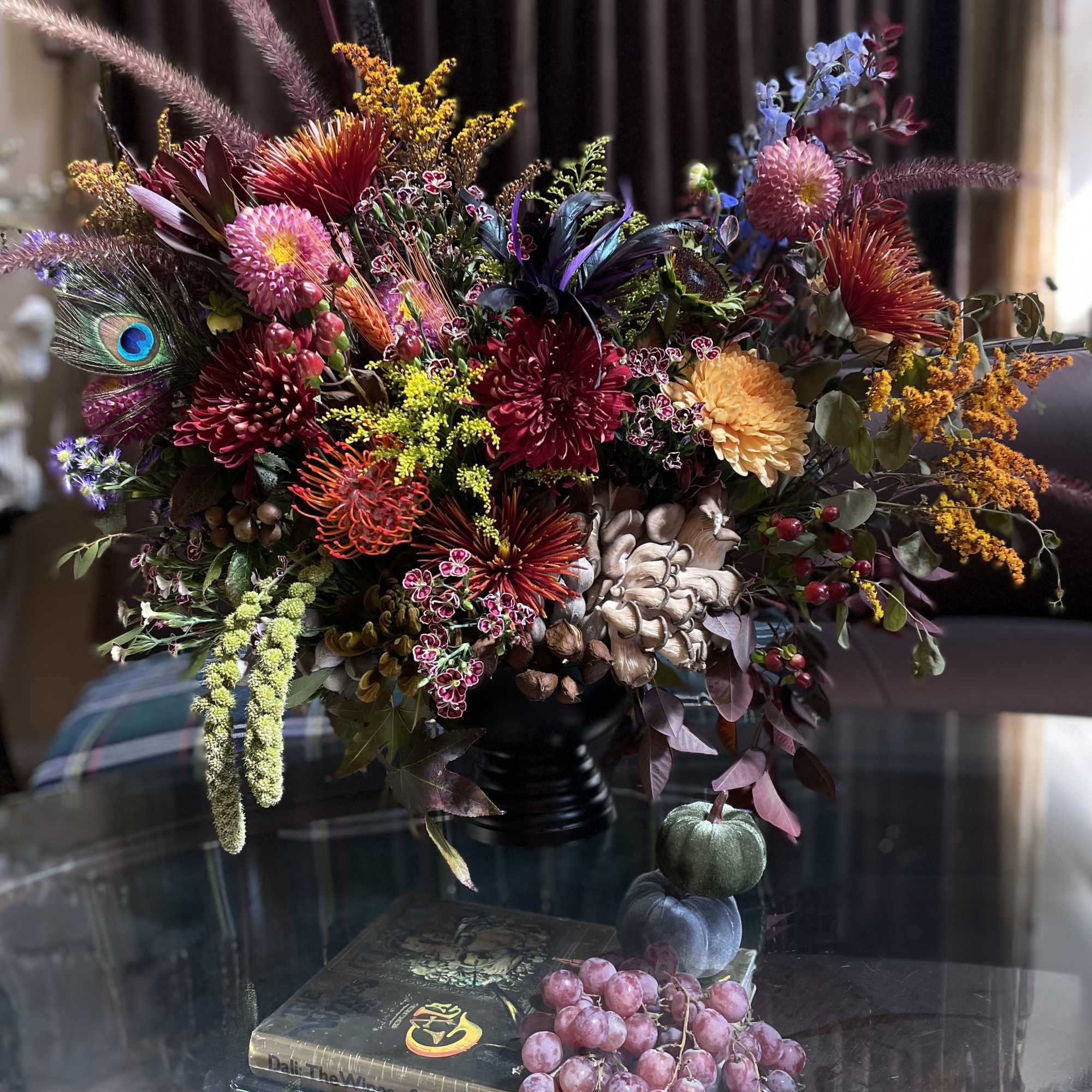 Colorful floral arrangement in a black vase with pumpkins and grapes