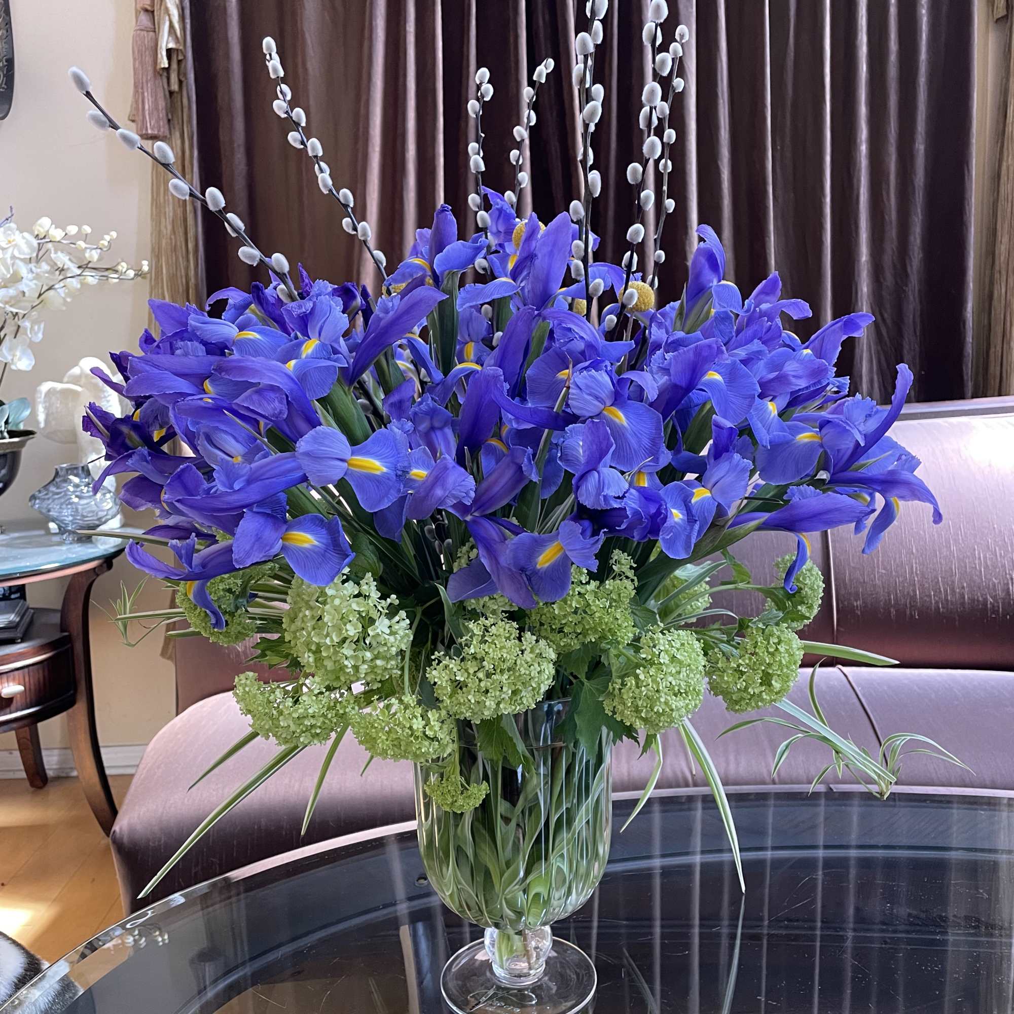 Blue iris arrangement in a clear glass vase with pussy willow stems