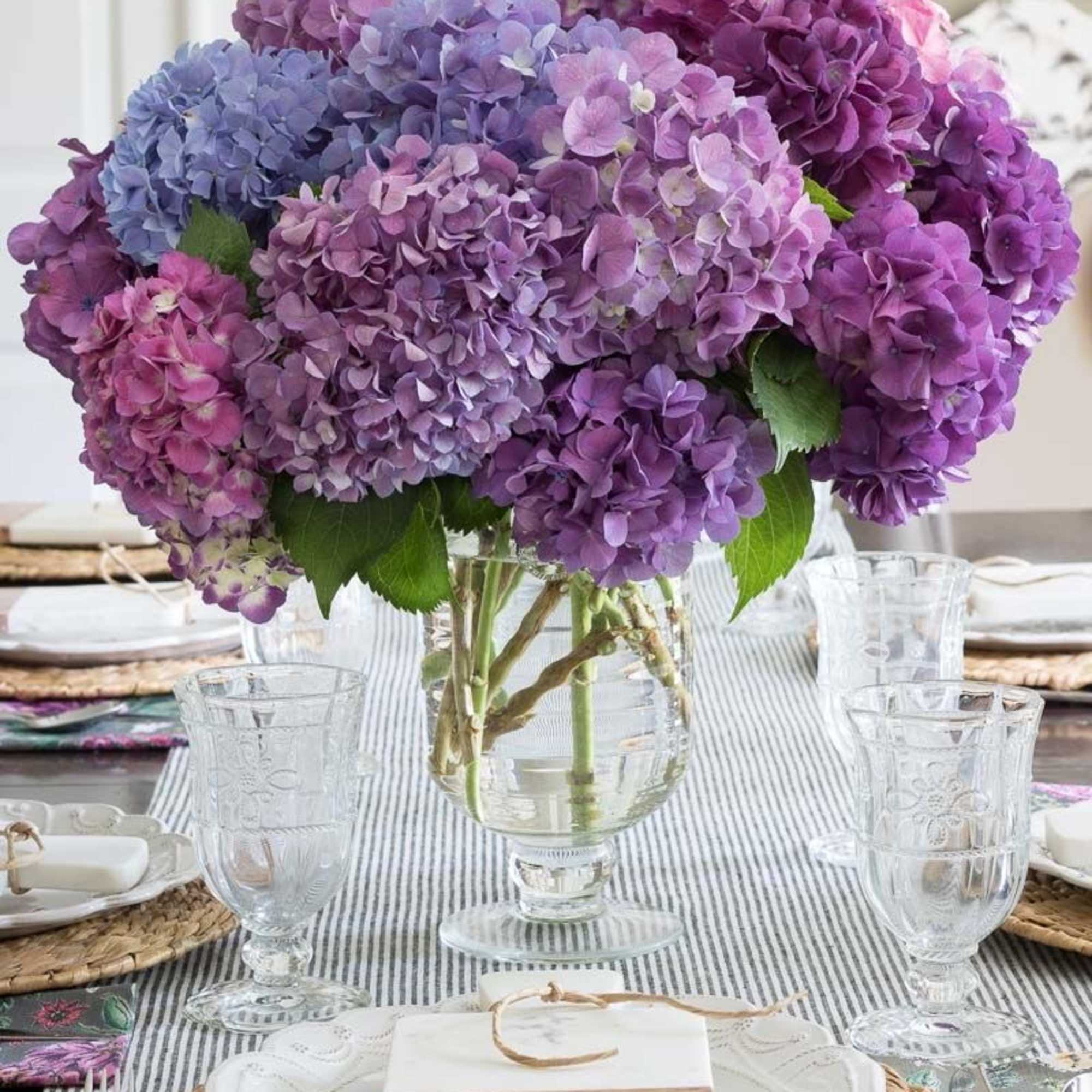 Purple and blue hydrangea centerpiece in a clear glass vase on a set table