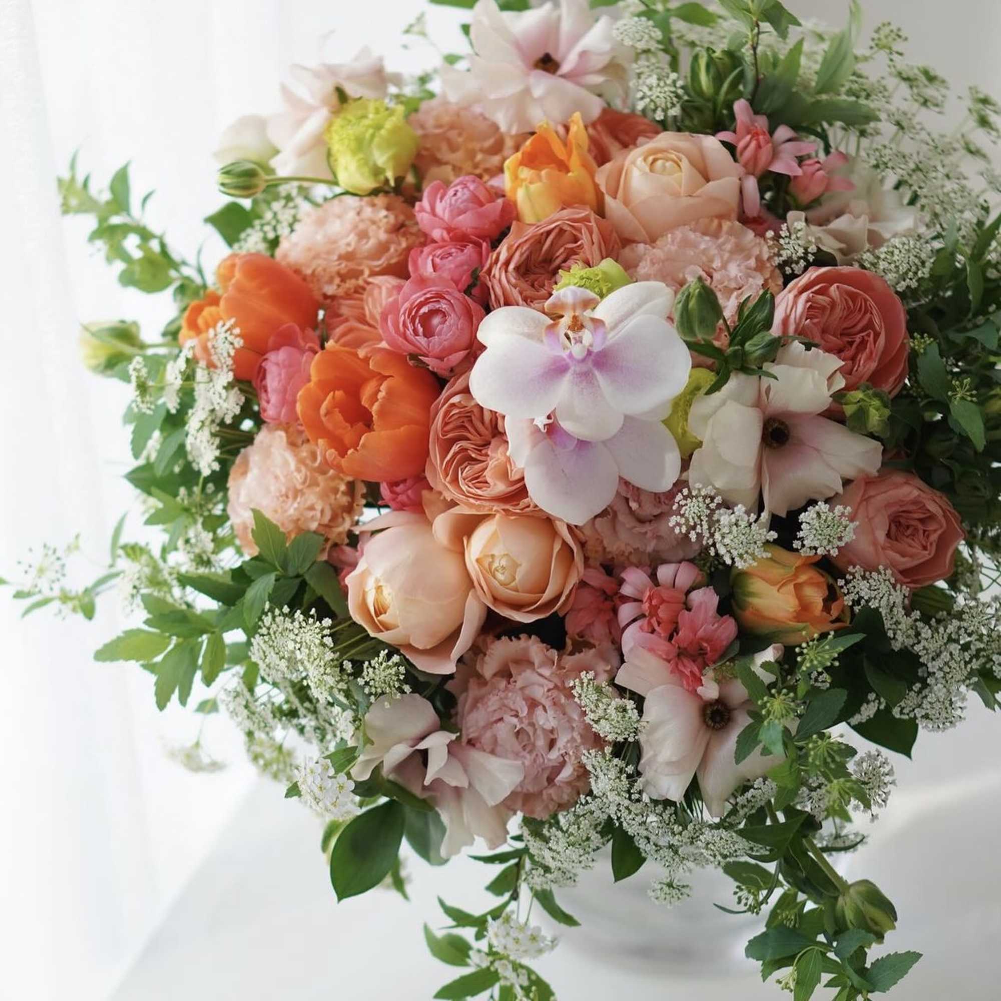 Round bouquet of peach, pink, and white flowers with greenery