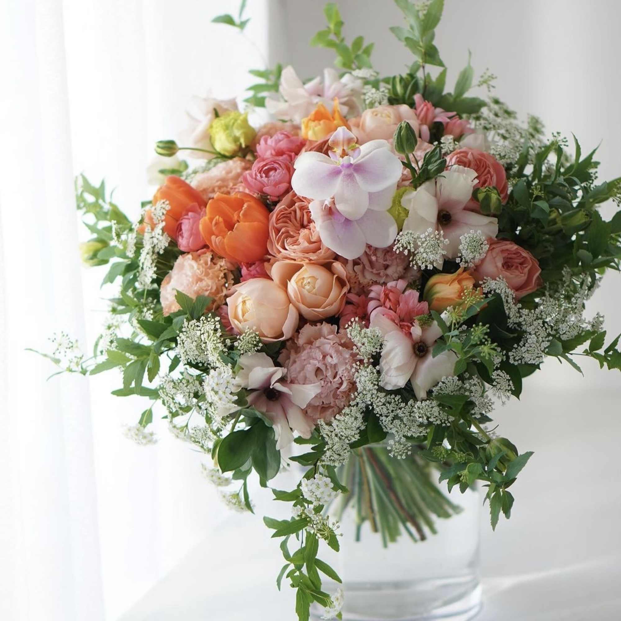 Mixed bouquet of pink, peach, and white flowers in a clear glass vase