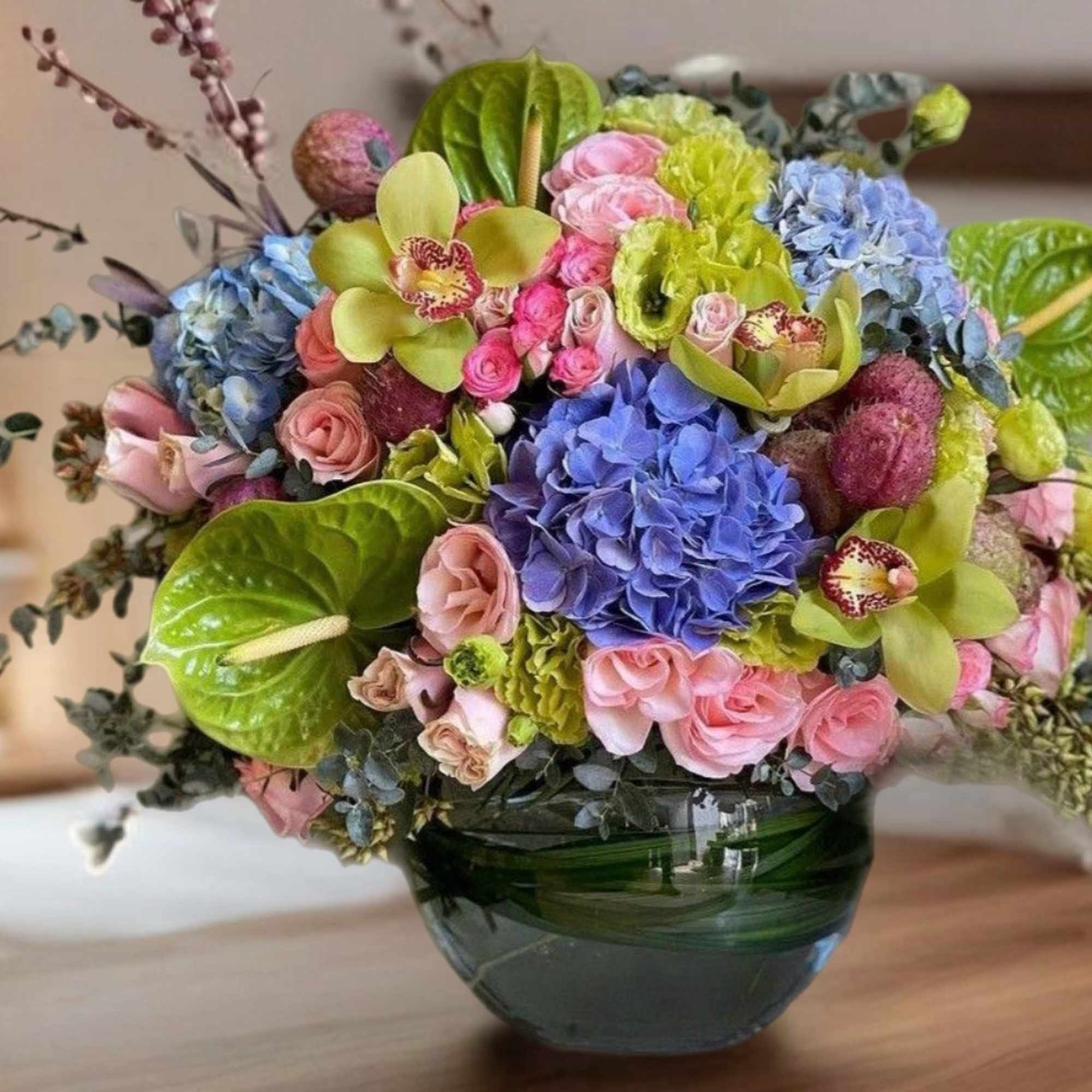 Colorful bouquet in a green glass vase with hydrangeas, roses, and orchids