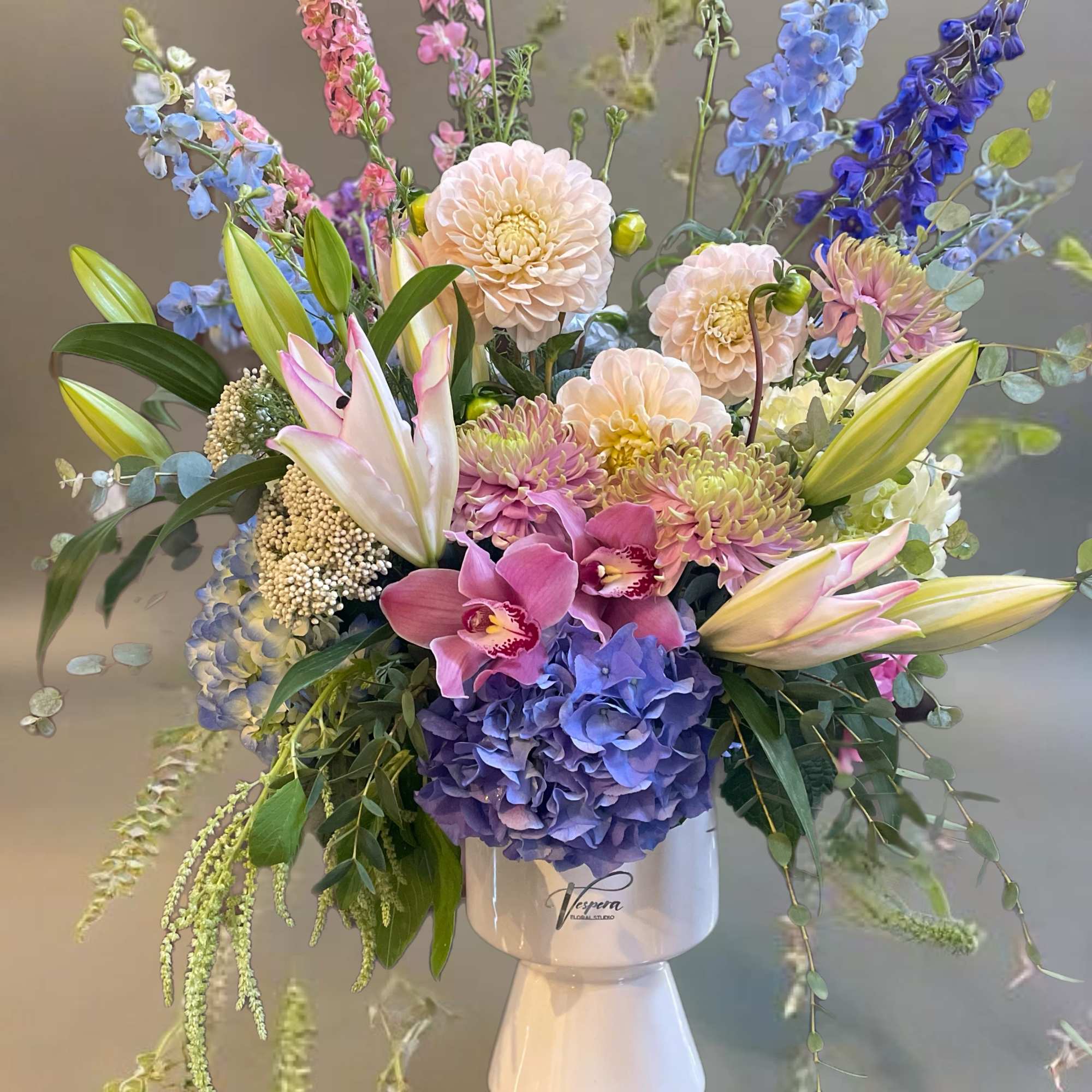 Mixed bouquet of pastel and blue flowers in a white pedestal vase