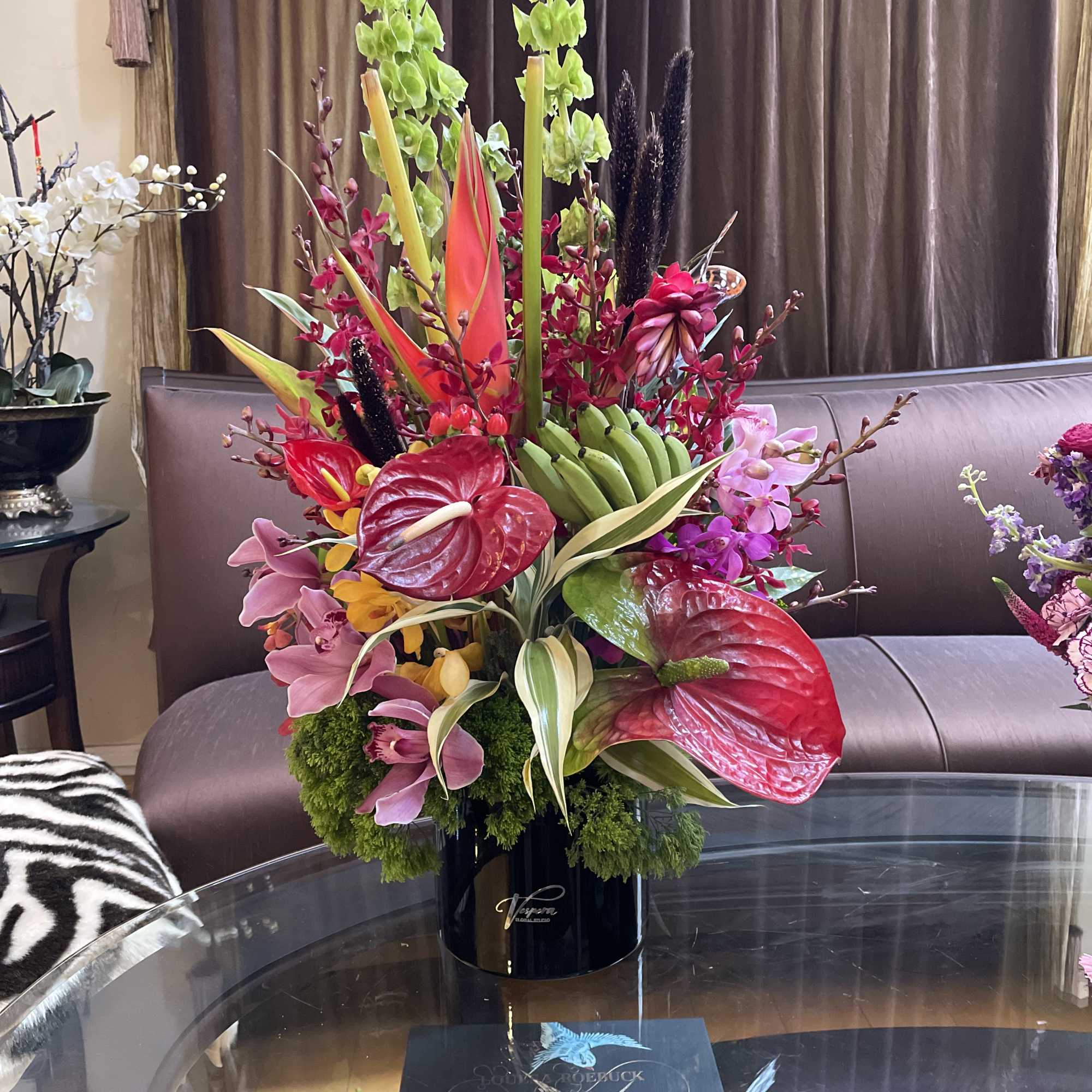 Tropical floral arrangement with orchids and red anthuriums in a black vase