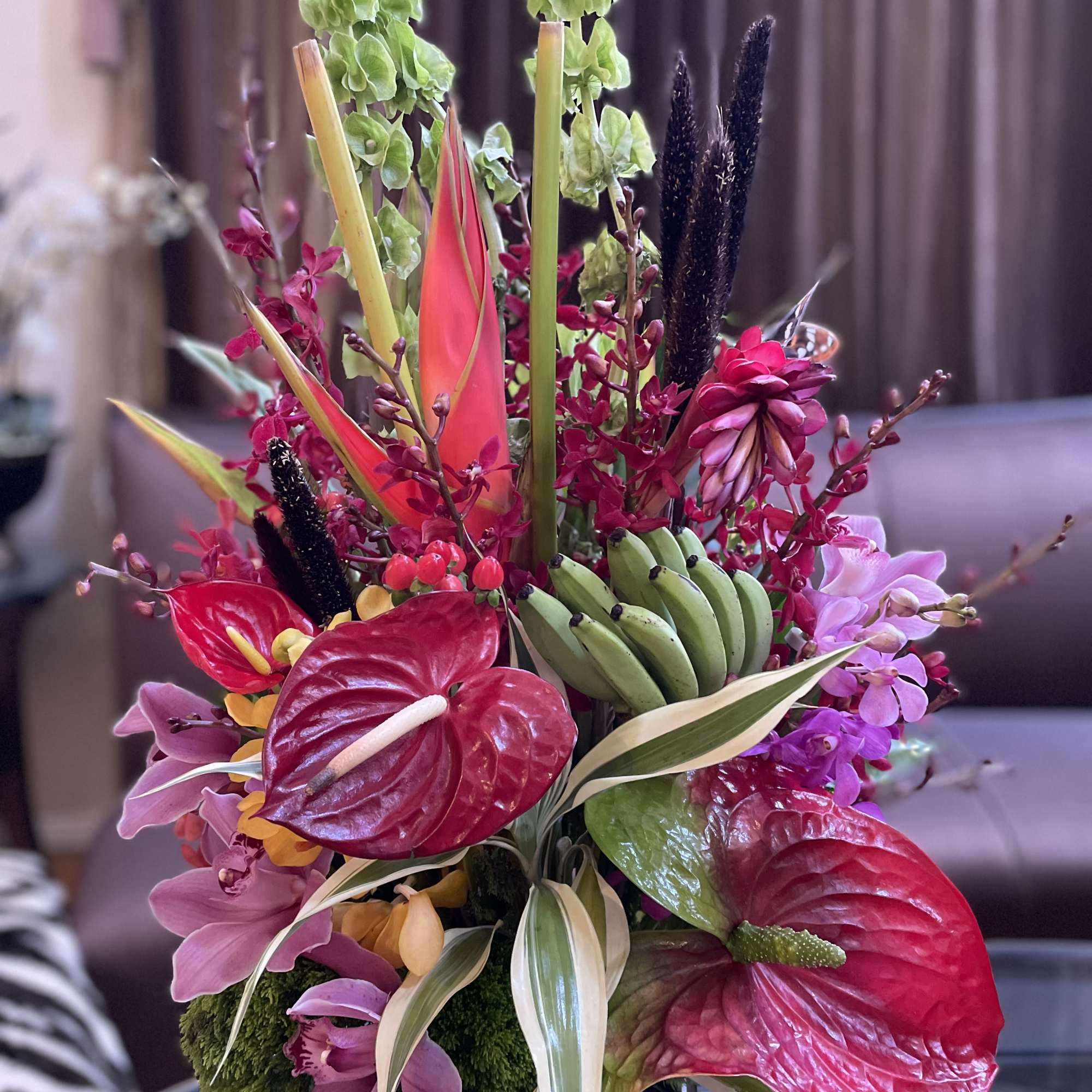 Tropical floral arrangement with pink anthuriums and orchids in a black vase