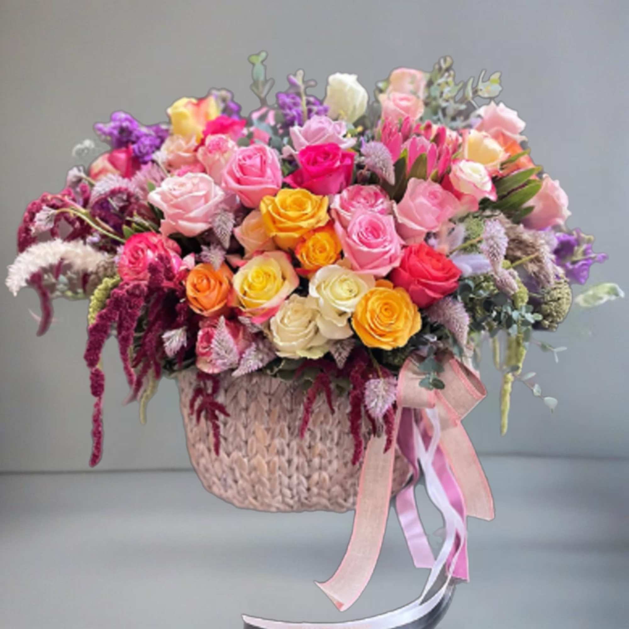 Mixed bouquet of colorful roses in a woven basket with ribbon