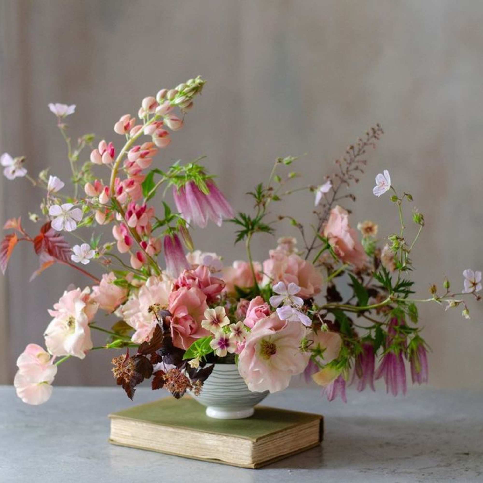 Loose pink and white flowers arranged in a small white vase on a book