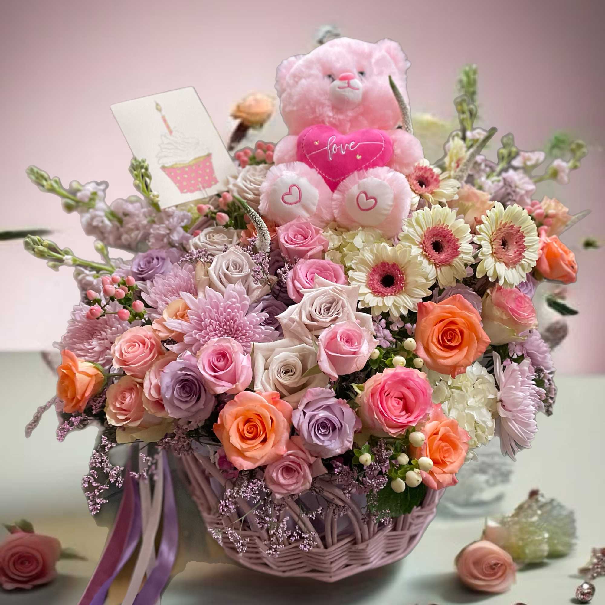 Pink teddy bear in a basket of roses and daisies with a love card