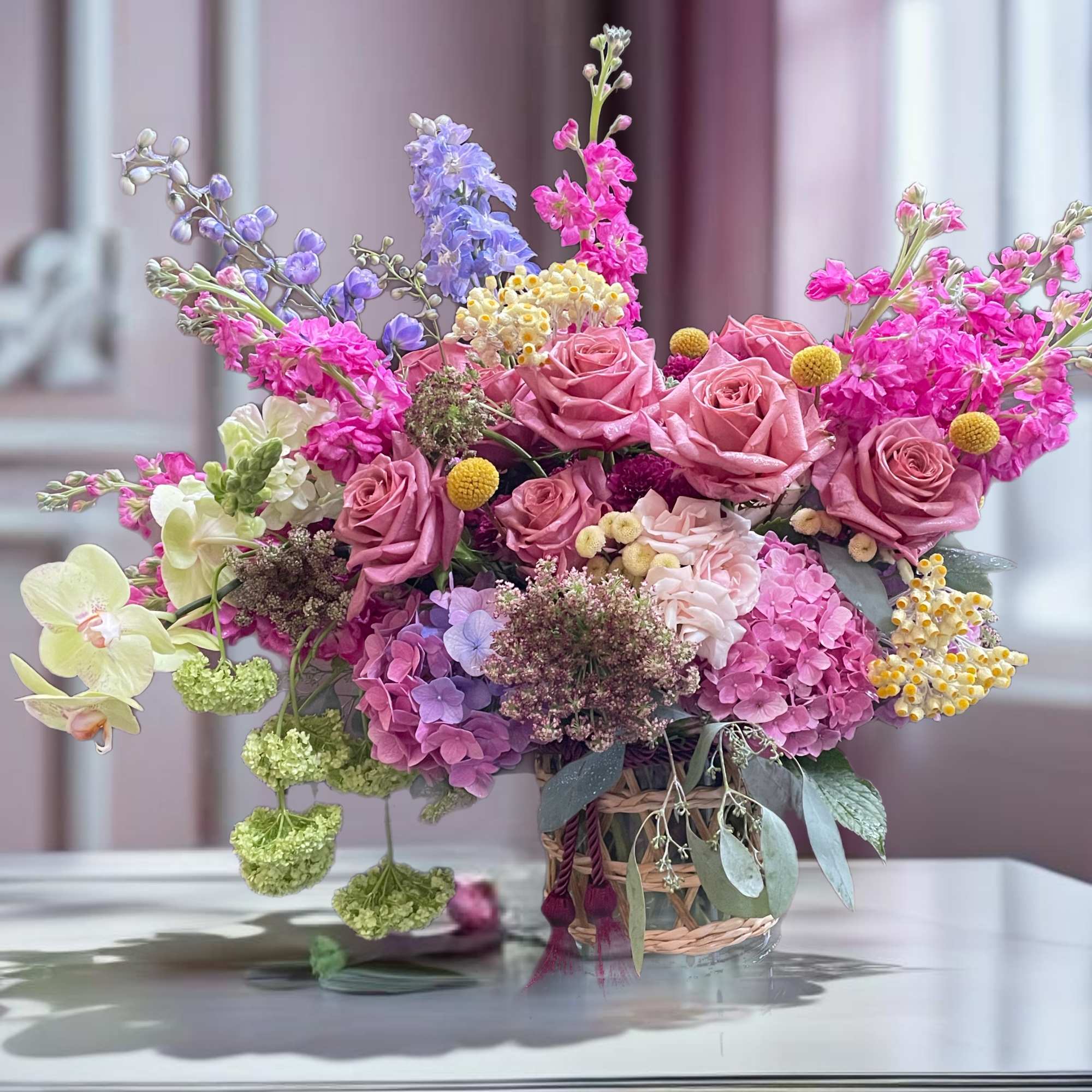 Mixed bouquet of pink roses, hydrangeas, and orchids in a basket vase