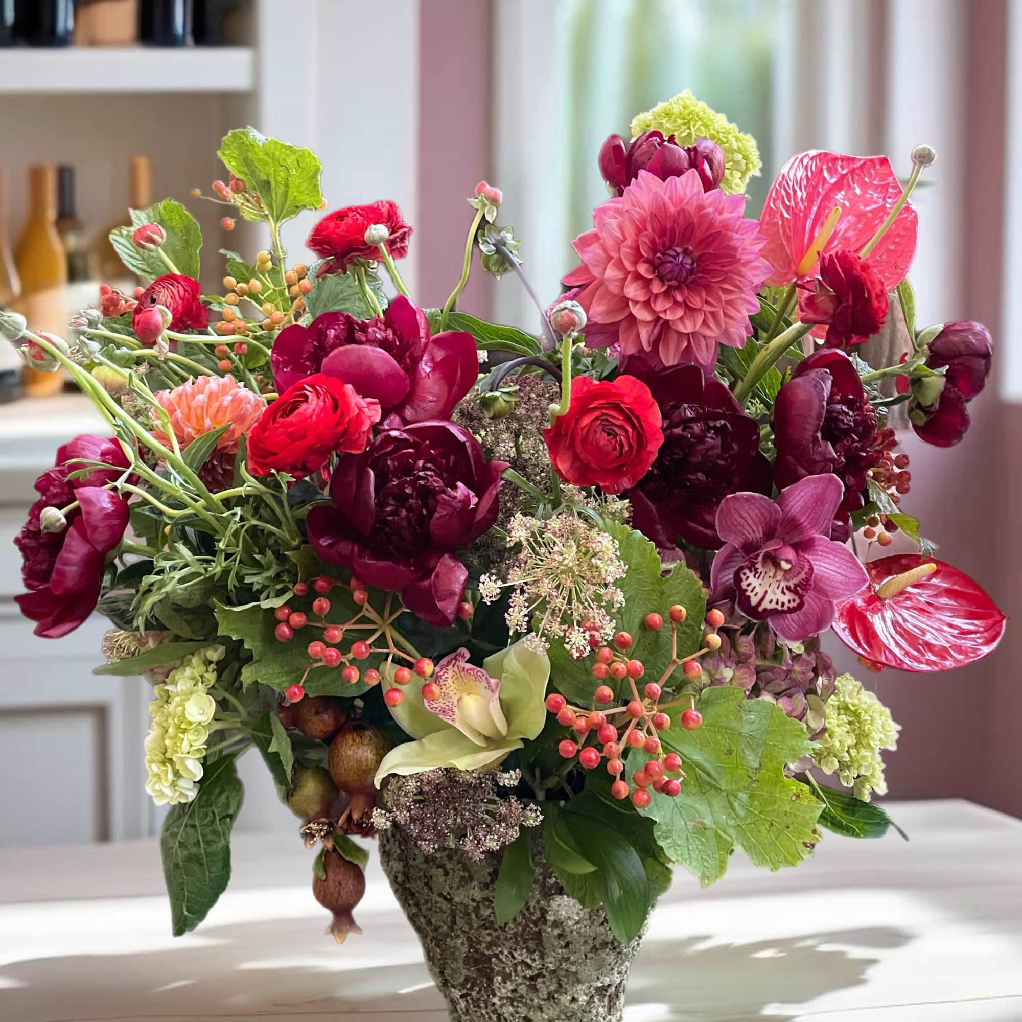 Lush mixed bouquet in a textured vase with pink, red, and burgundy blooms