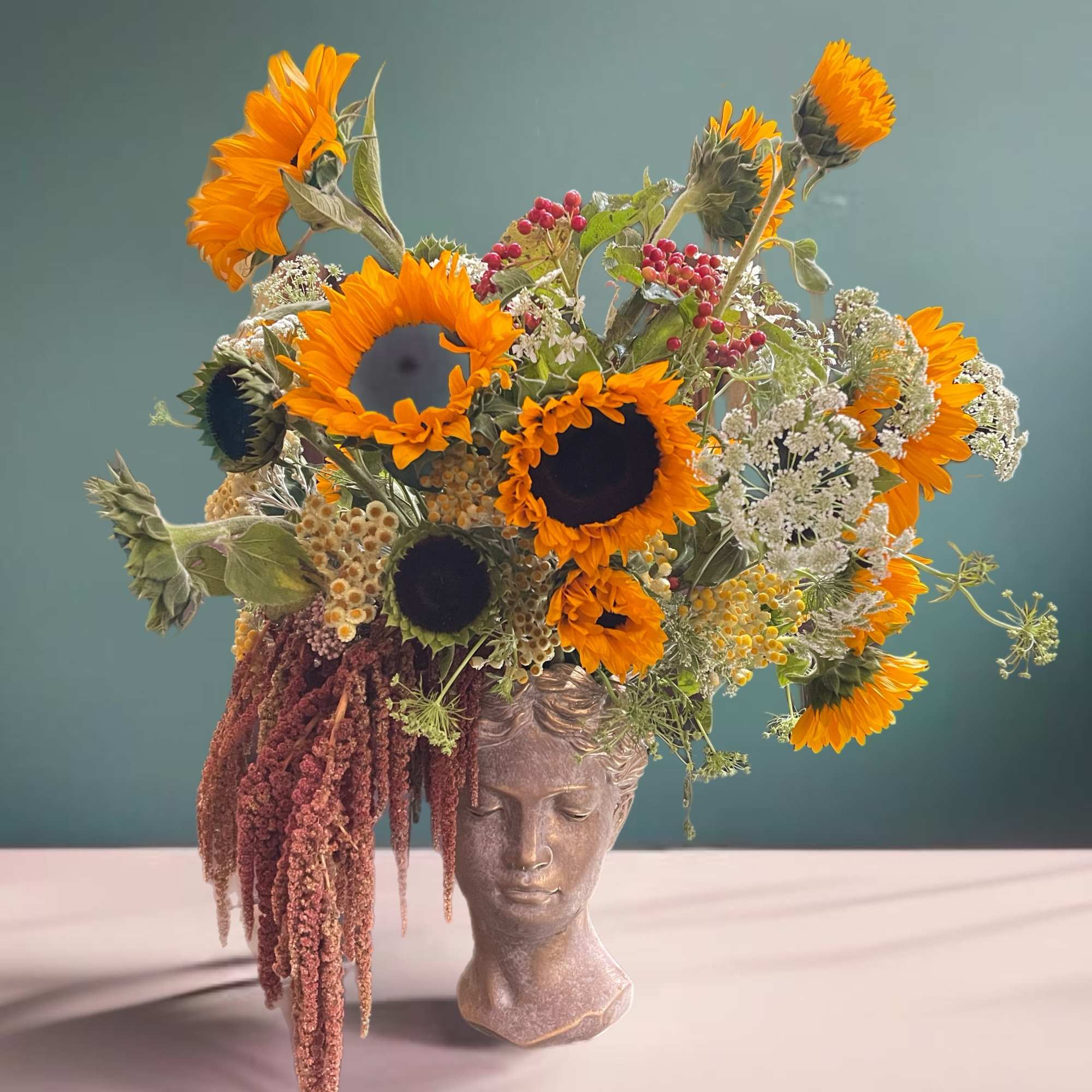 Sunflower arrangement in a sculpted bust vase with trailing burgundy flowers
