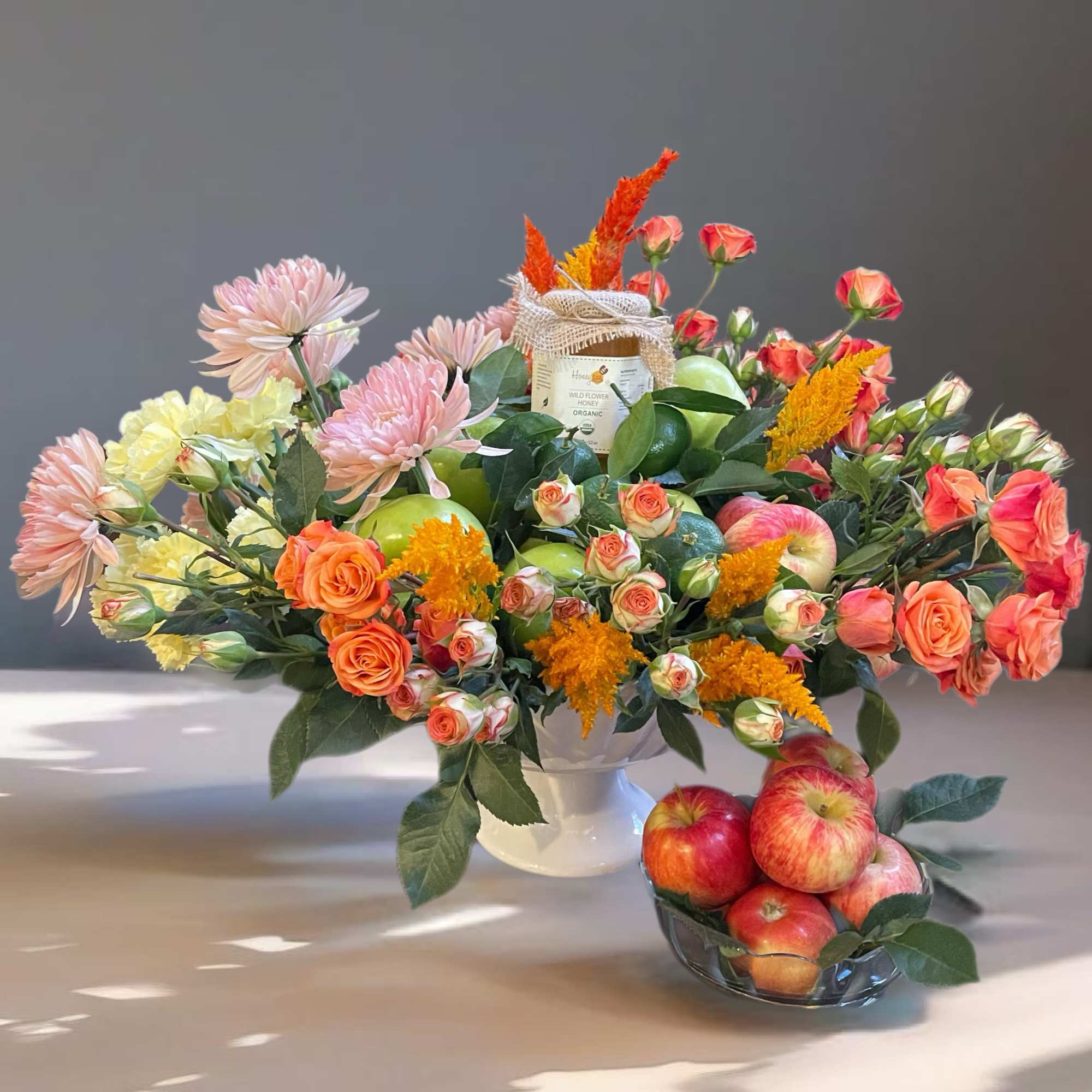 Mixed bouquet in a white vase with apples and a small bowl of apples