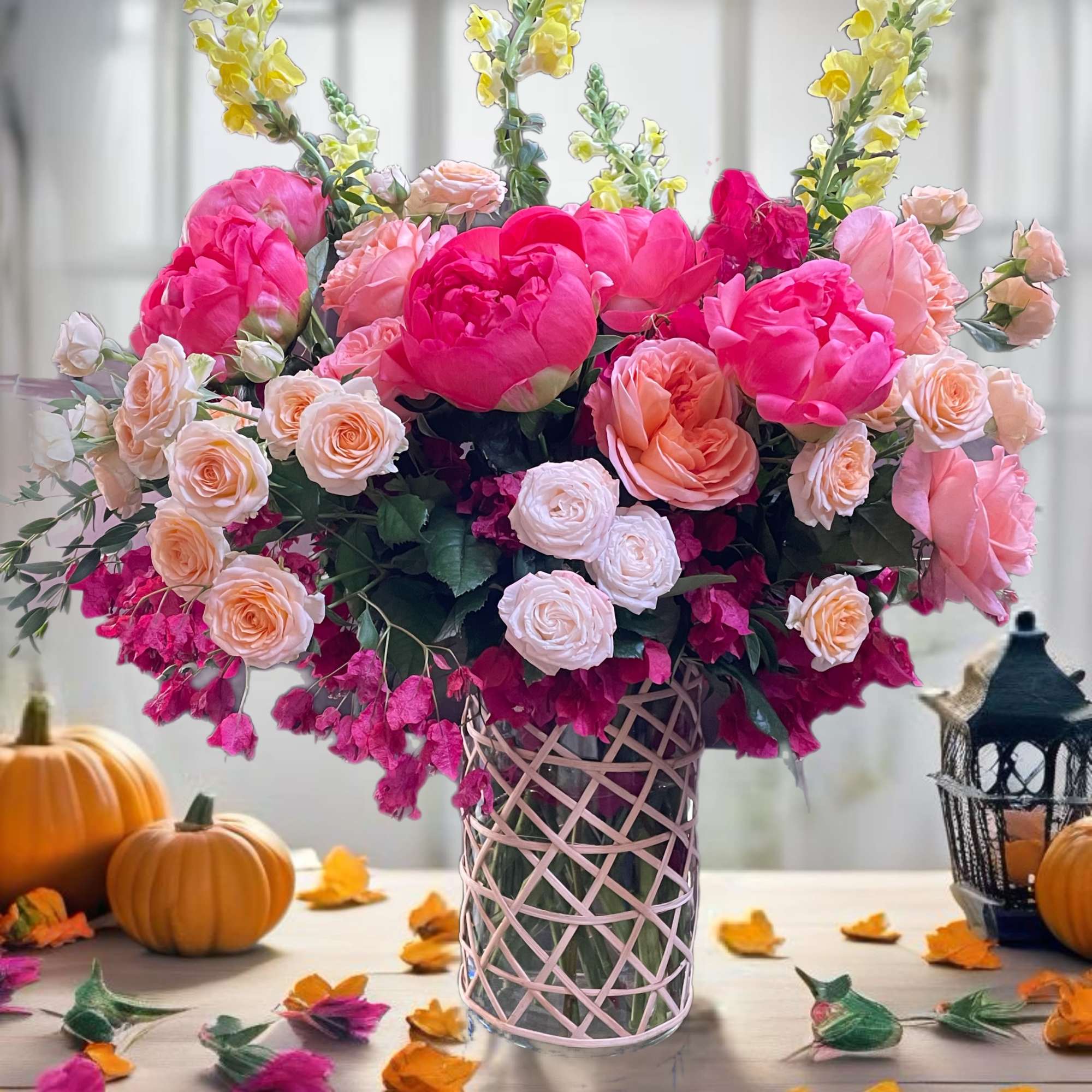 Pink and peach floral arrangement in a glass vase with pumpkins and fall leaves