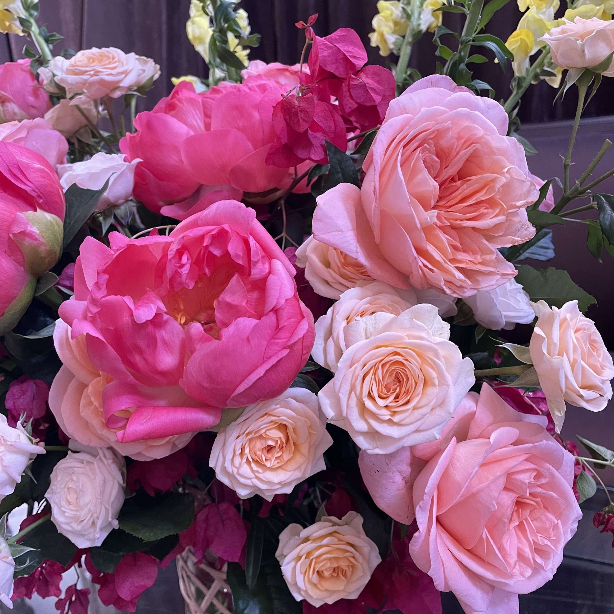 Pink and peach roses arranged in a woven vase with yellow snapdragons