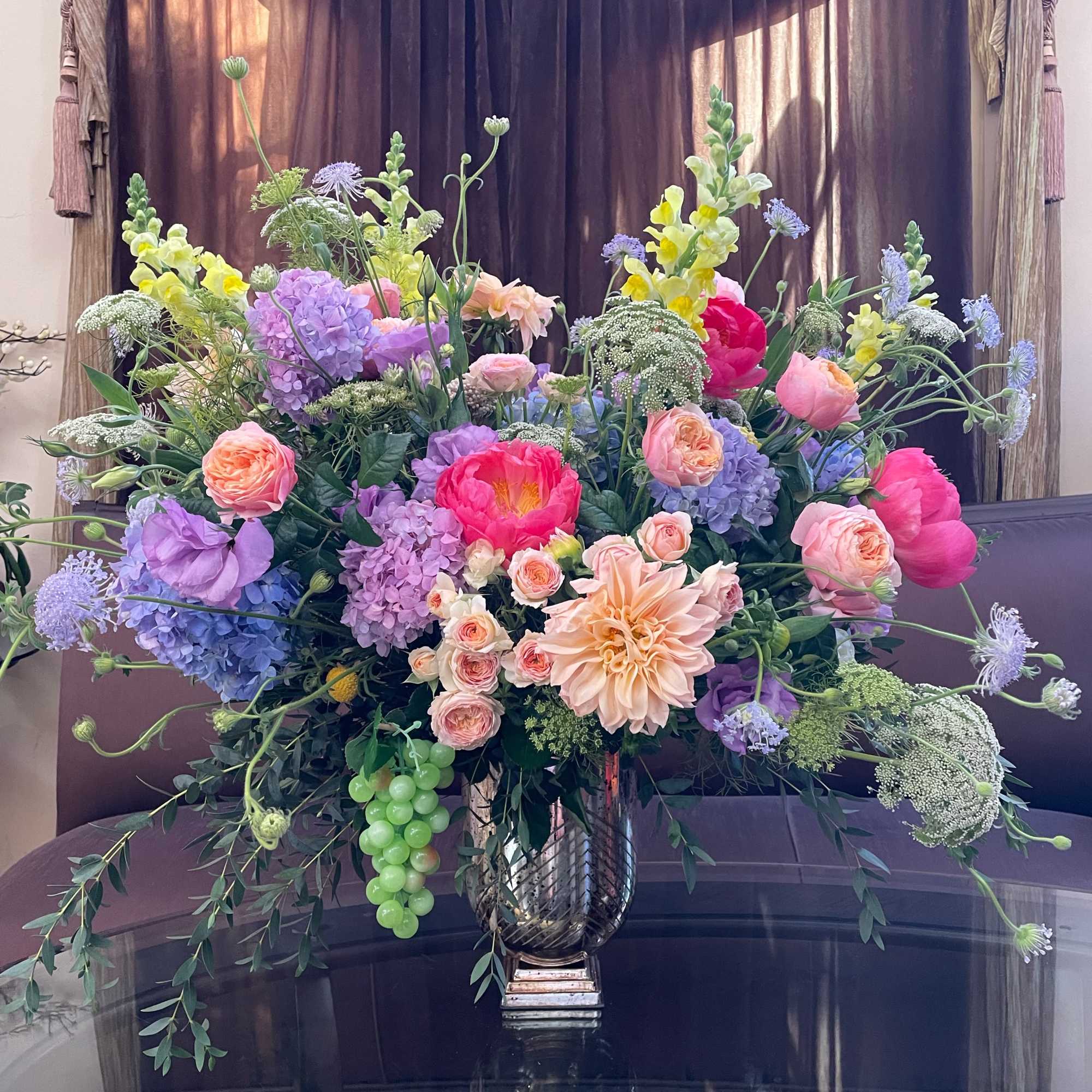 Large mixed bouquet in a silver vase with pink, purple, yellow, and peach flowers