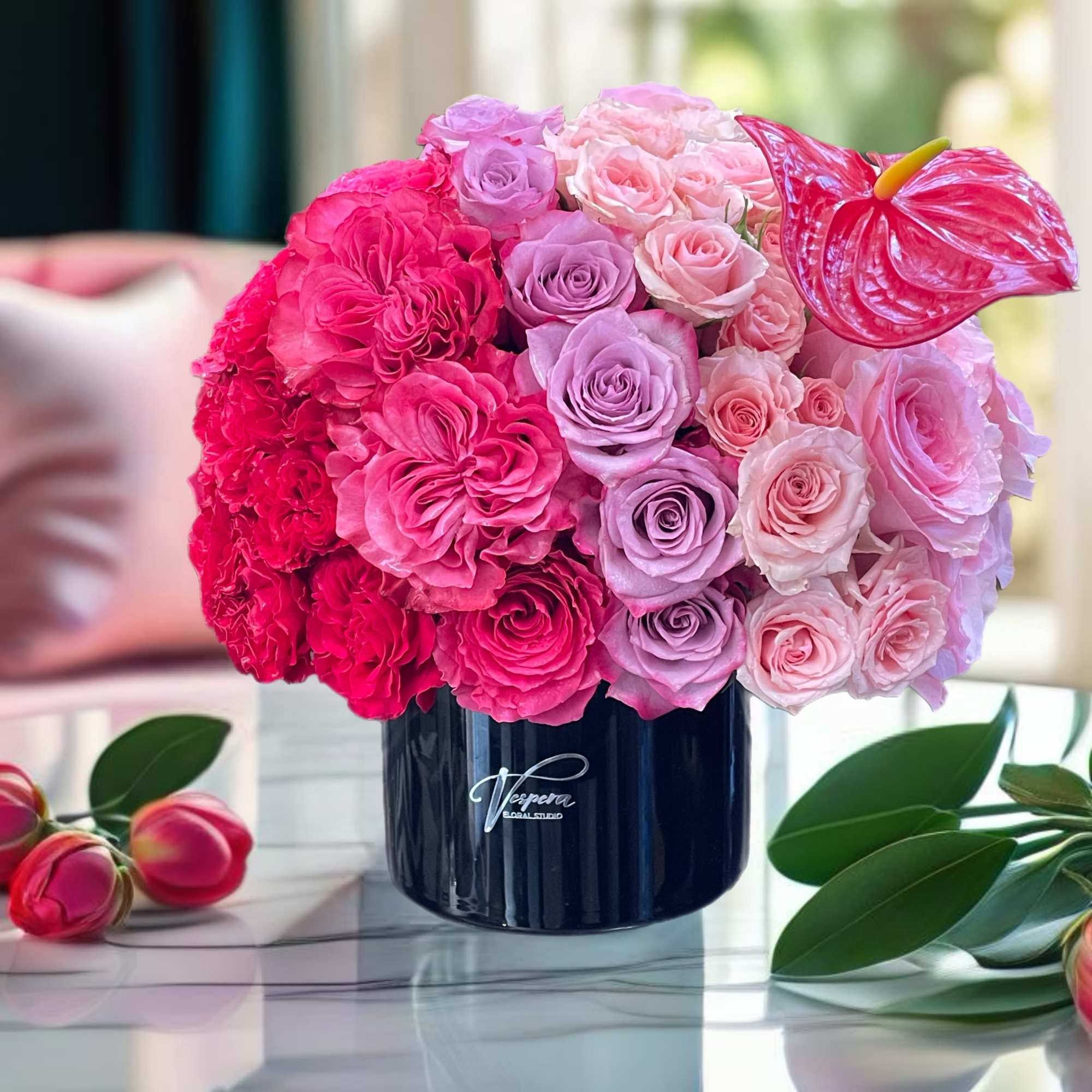 Pink and lavender rose arrangement in a dark vase with an anthurium bloom