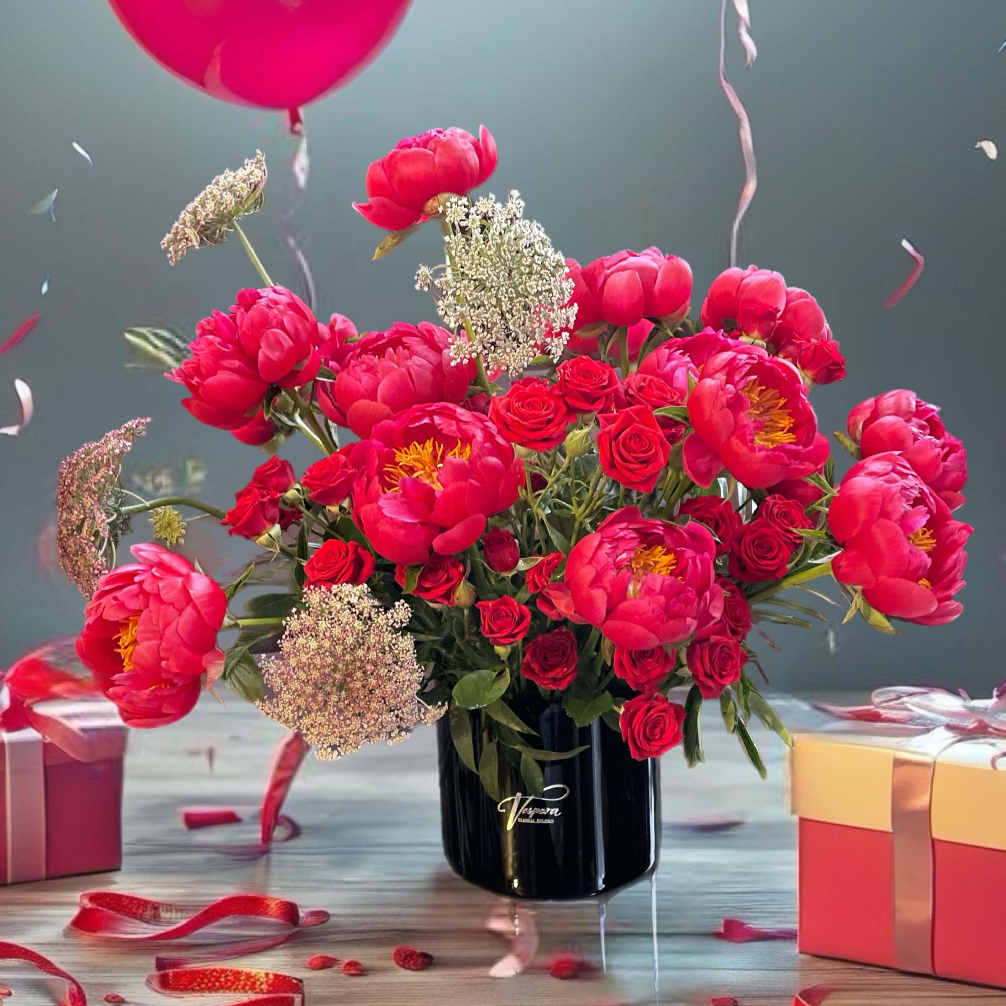 Pink peonies and red roses in a black vase with balloons and gift boxes