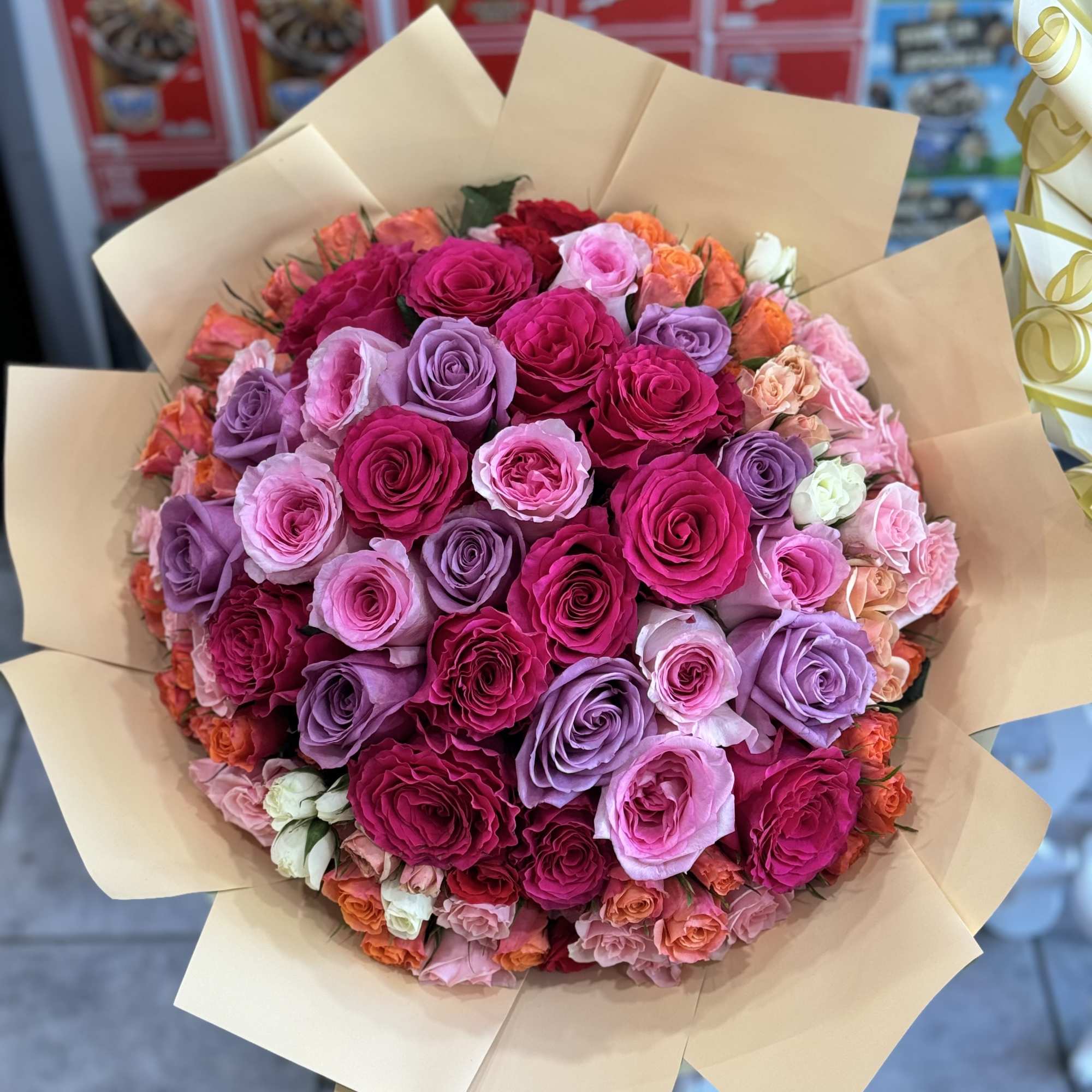 Large bouquet of pink, purple, and orange roses wrapped in tan paper