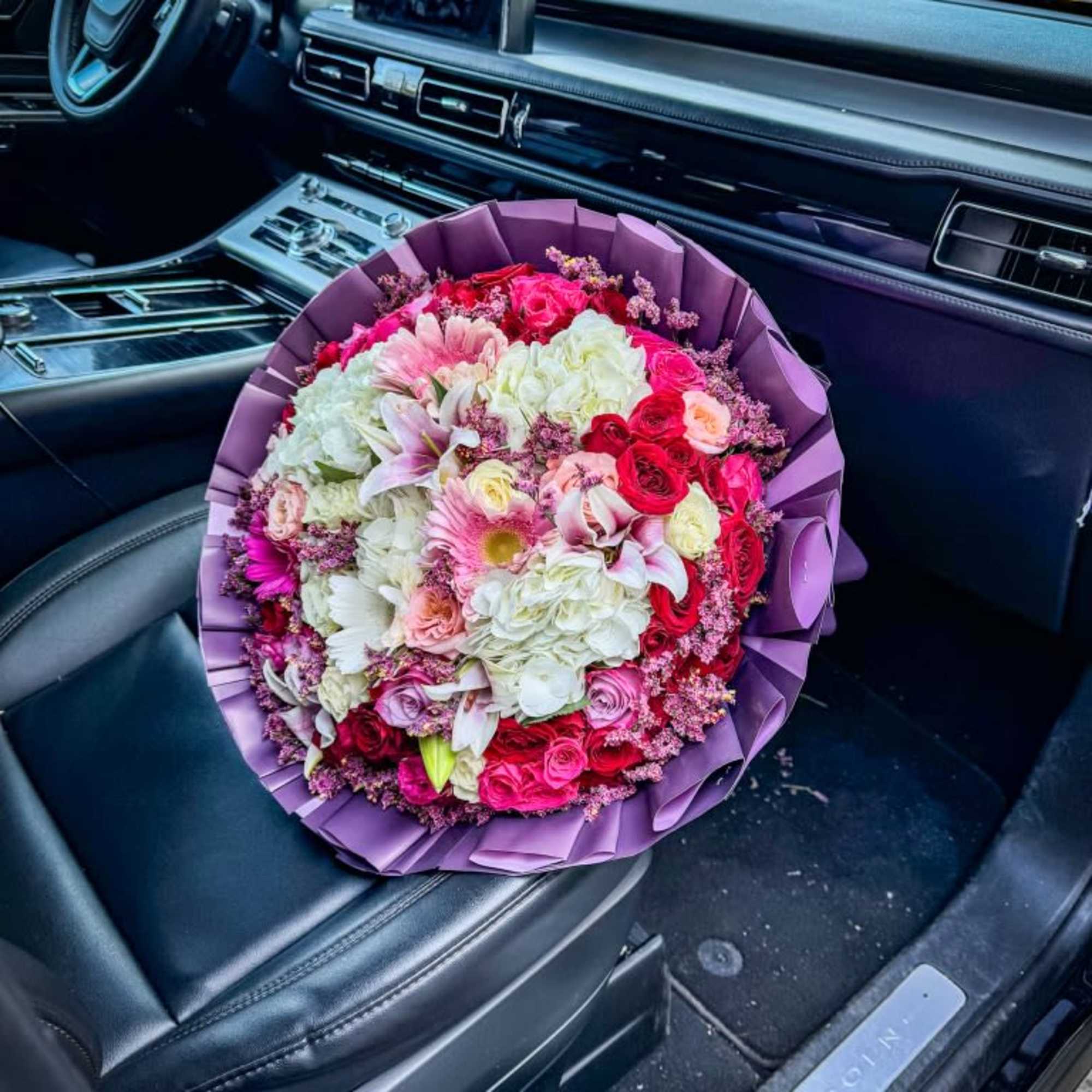 Large bouquet of pink, white, and red flowers wrapped in purple paper