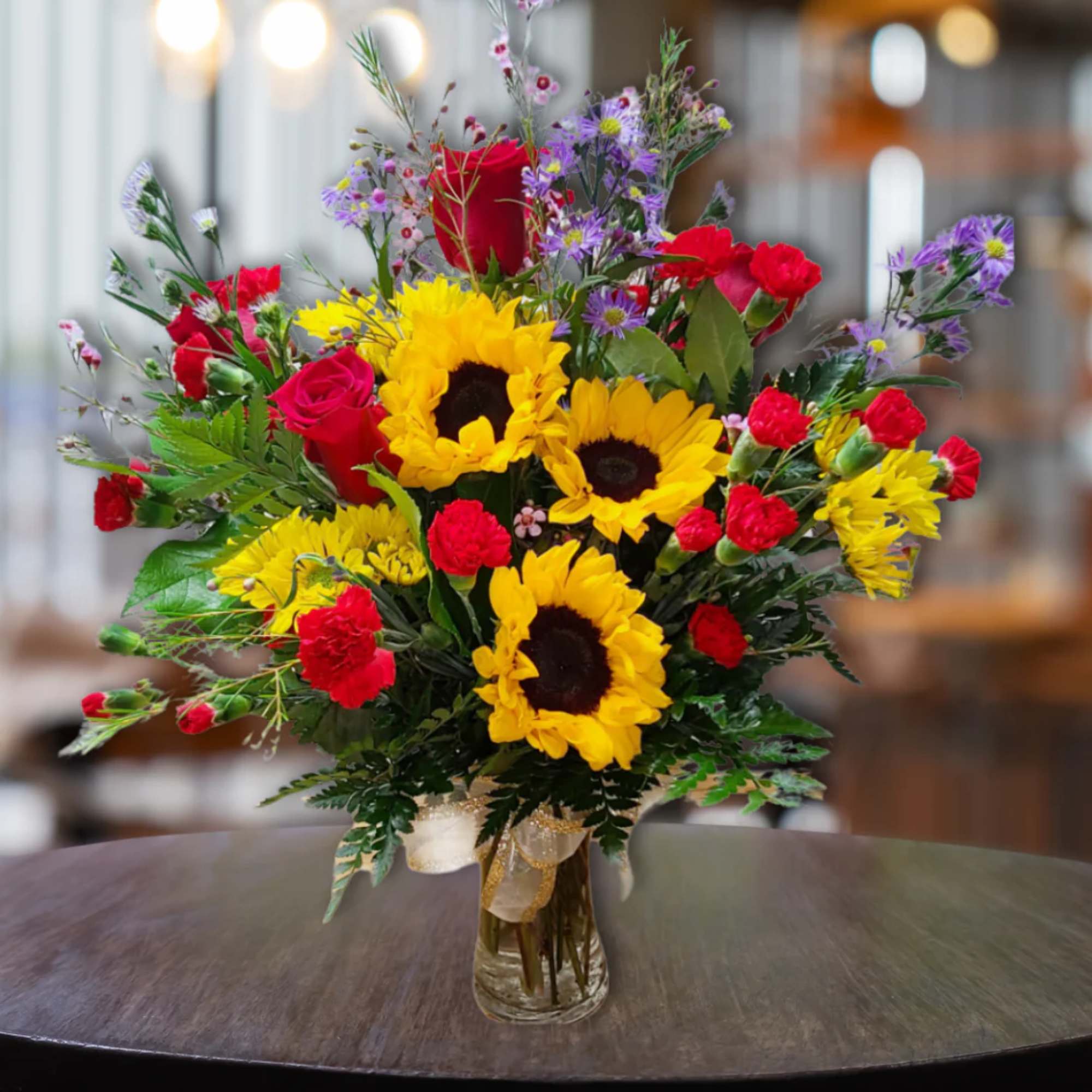 Bouquet of sunflowers, red roses, and purple daisies in a glass vase