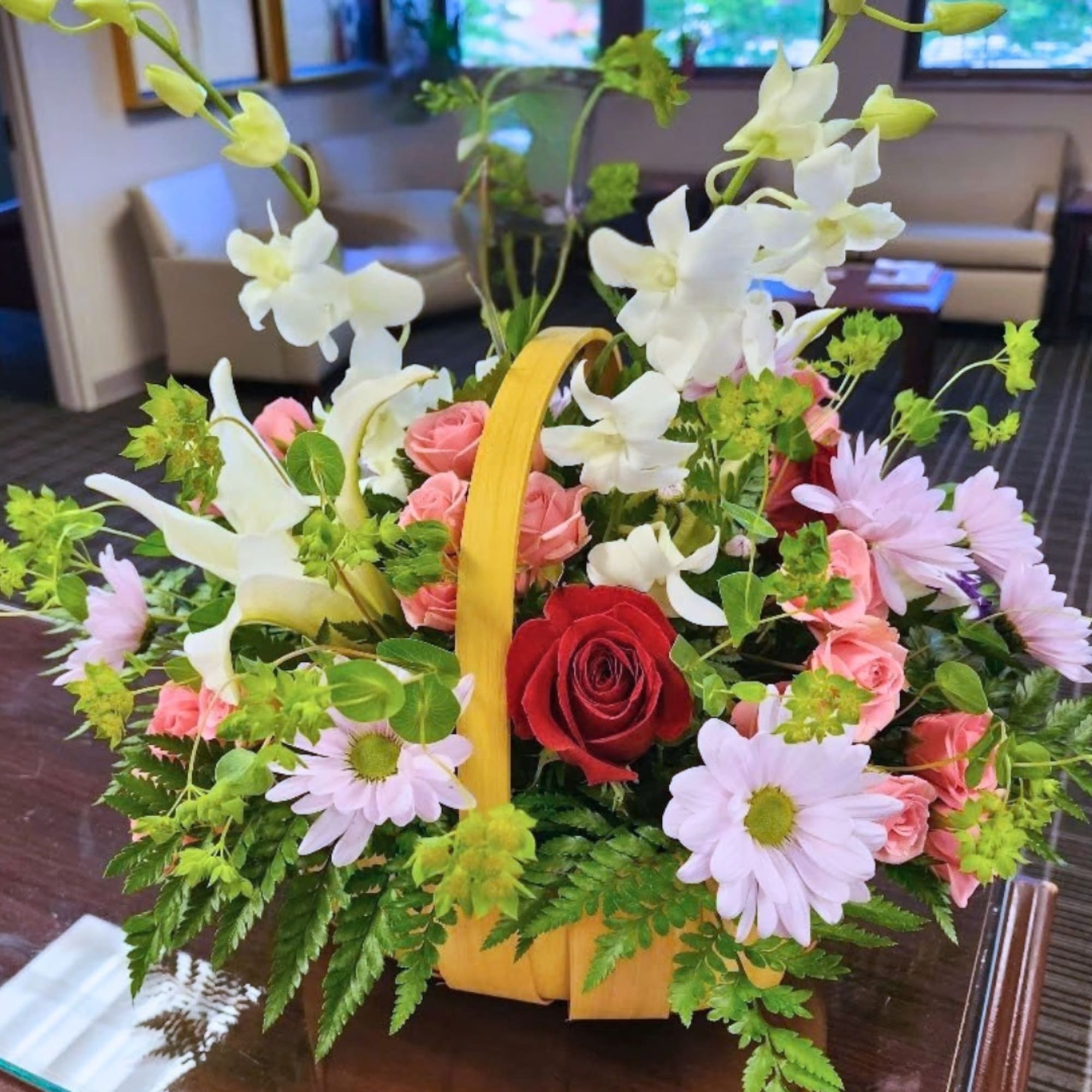 Basket arrangement with red and pink roses, white orchids, and pale daisies