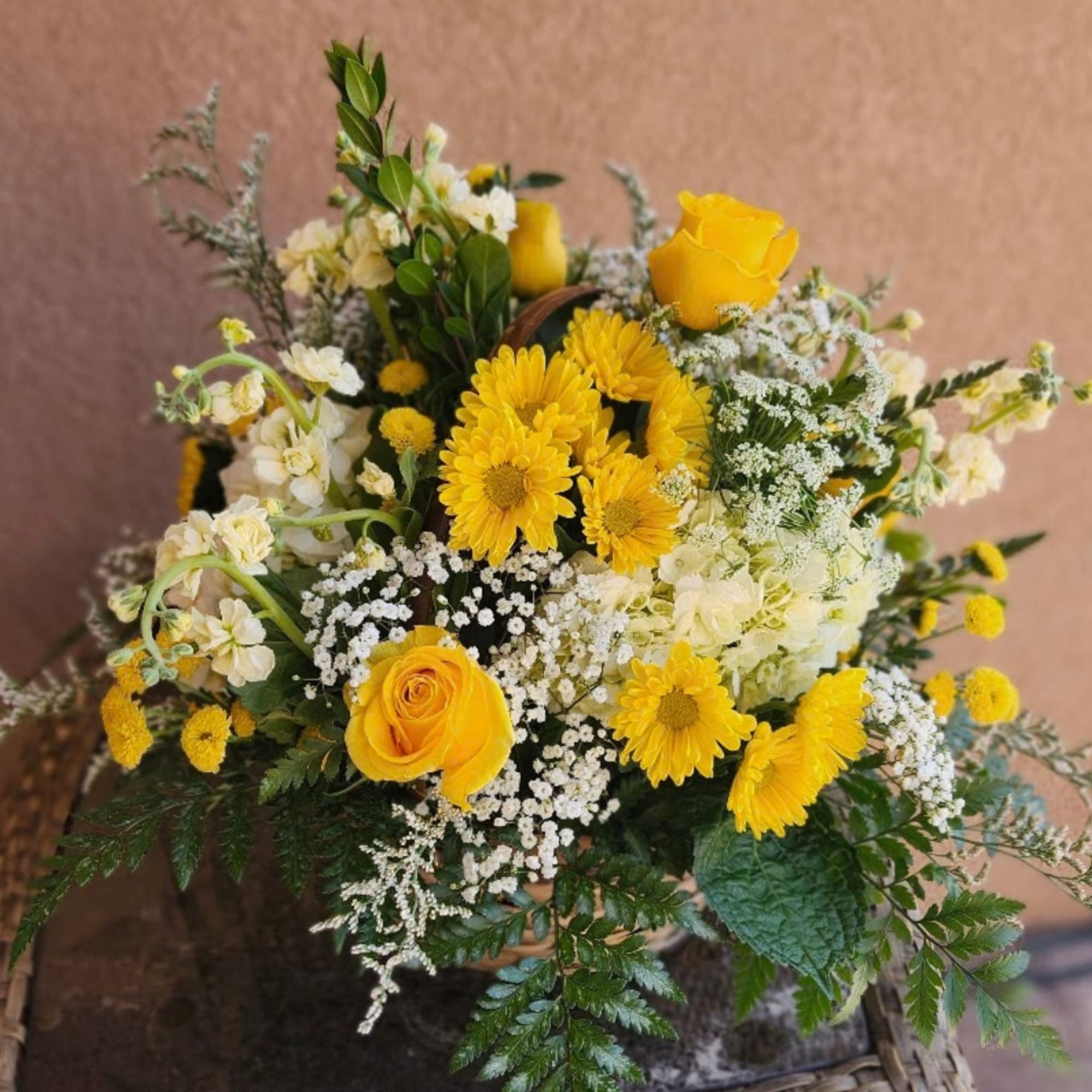 Yellow roses and daisies arranged with white filler flowers in a basket