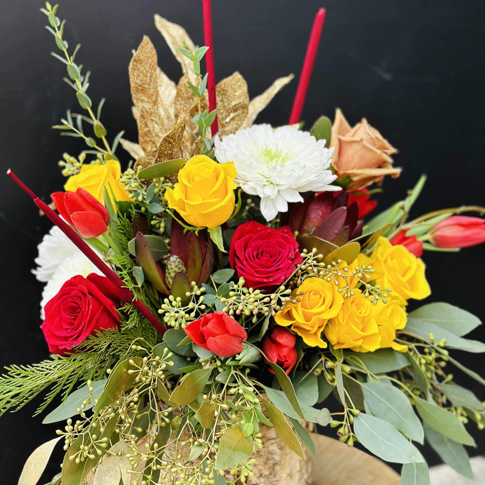 Mixed bouquet of red, yellow, and white flowers in a rustic container