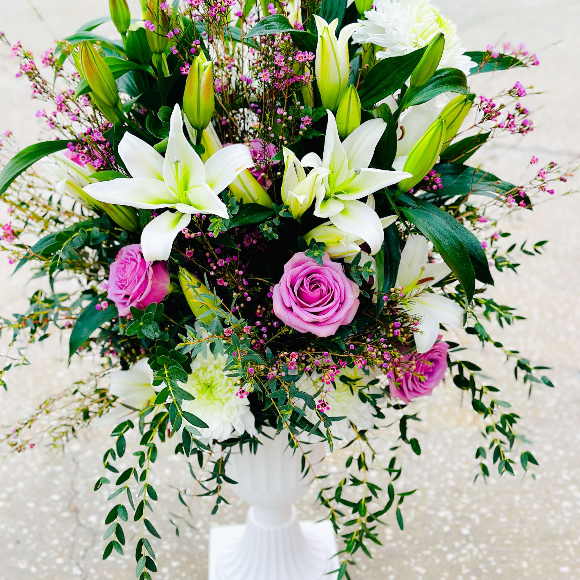 White lilies and pink roses arranged in a white pedestal vase