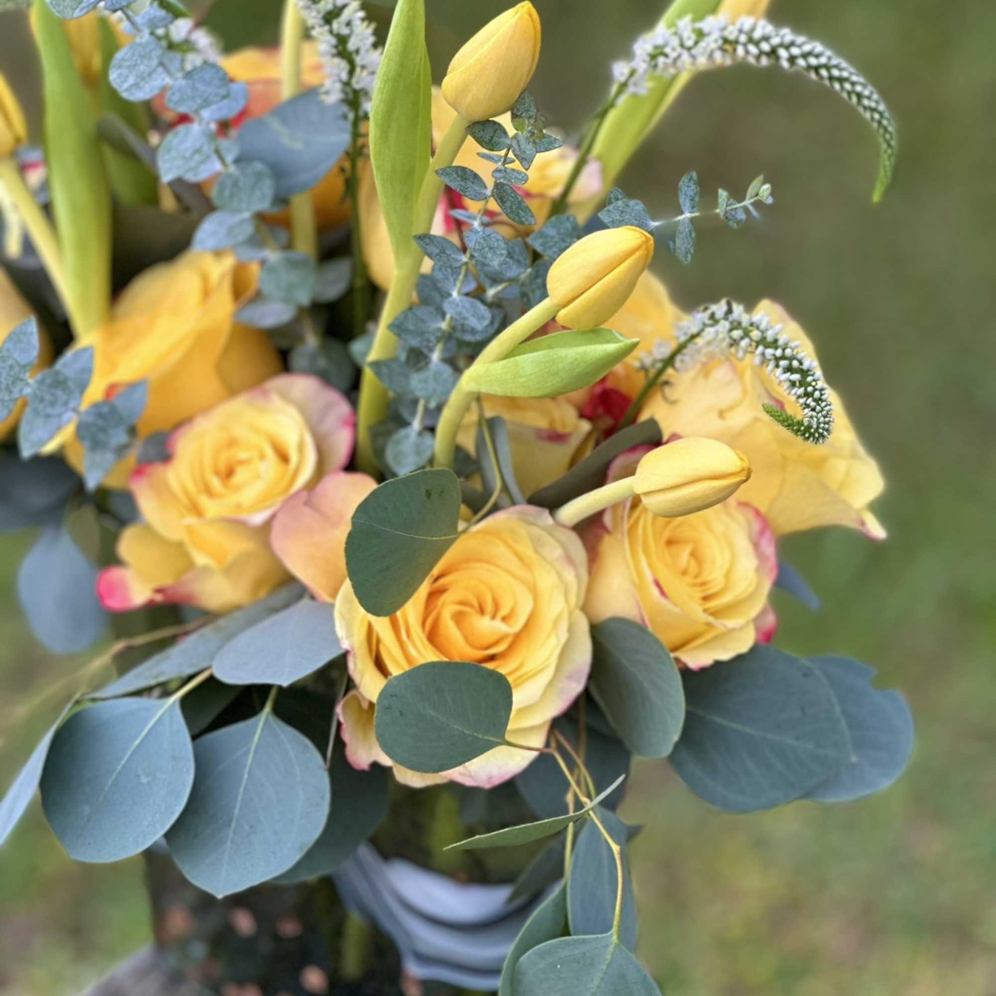 Yellow roses and tulips arranged with blue eucalyptus in a bouquet
