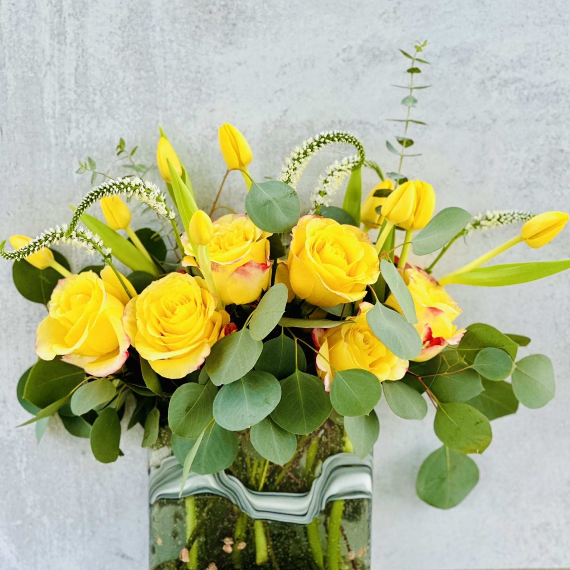 Yellow roses and tulips in a square glass vase