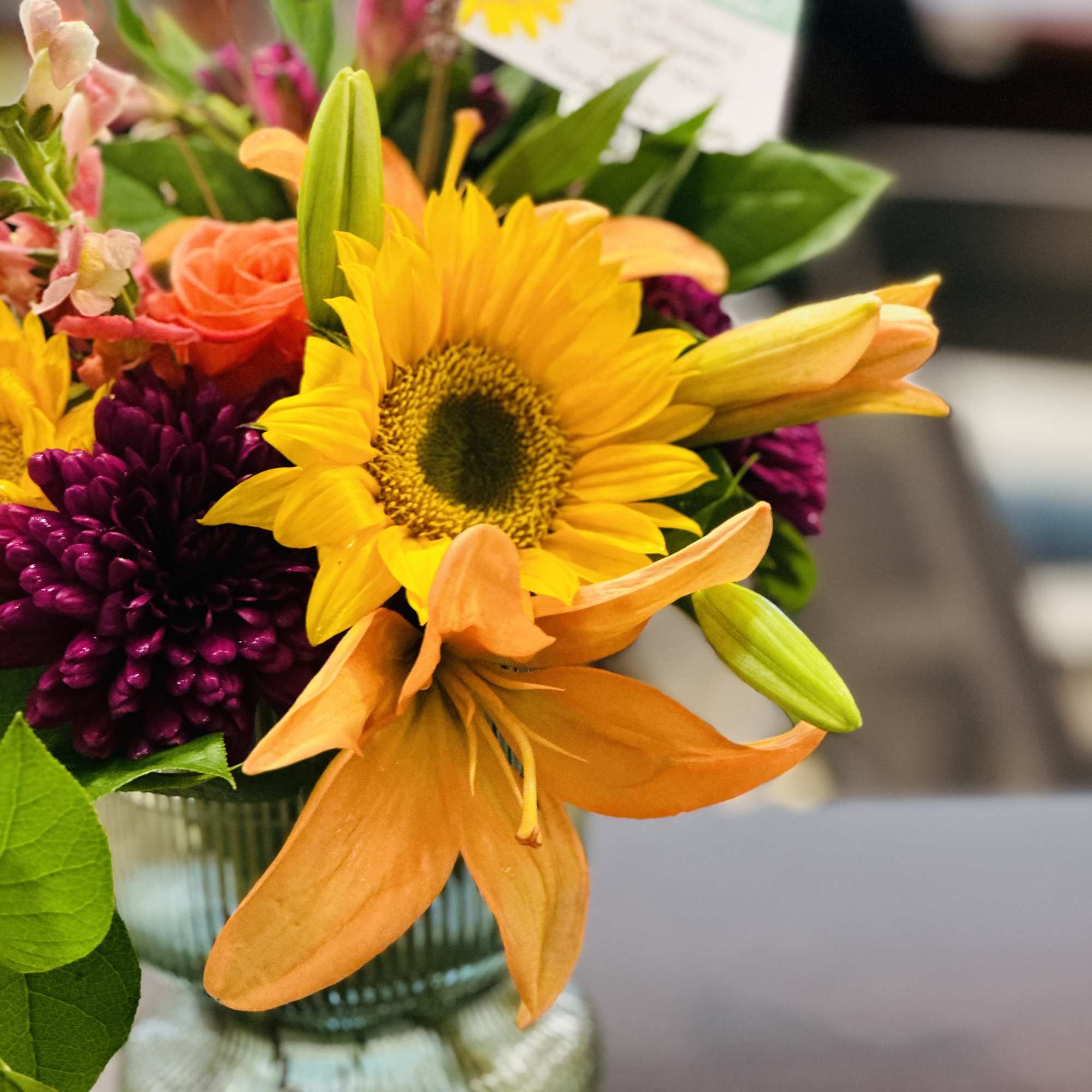 Bouquet with a sunflower, orange lily, and purple blooms in a glass vase
