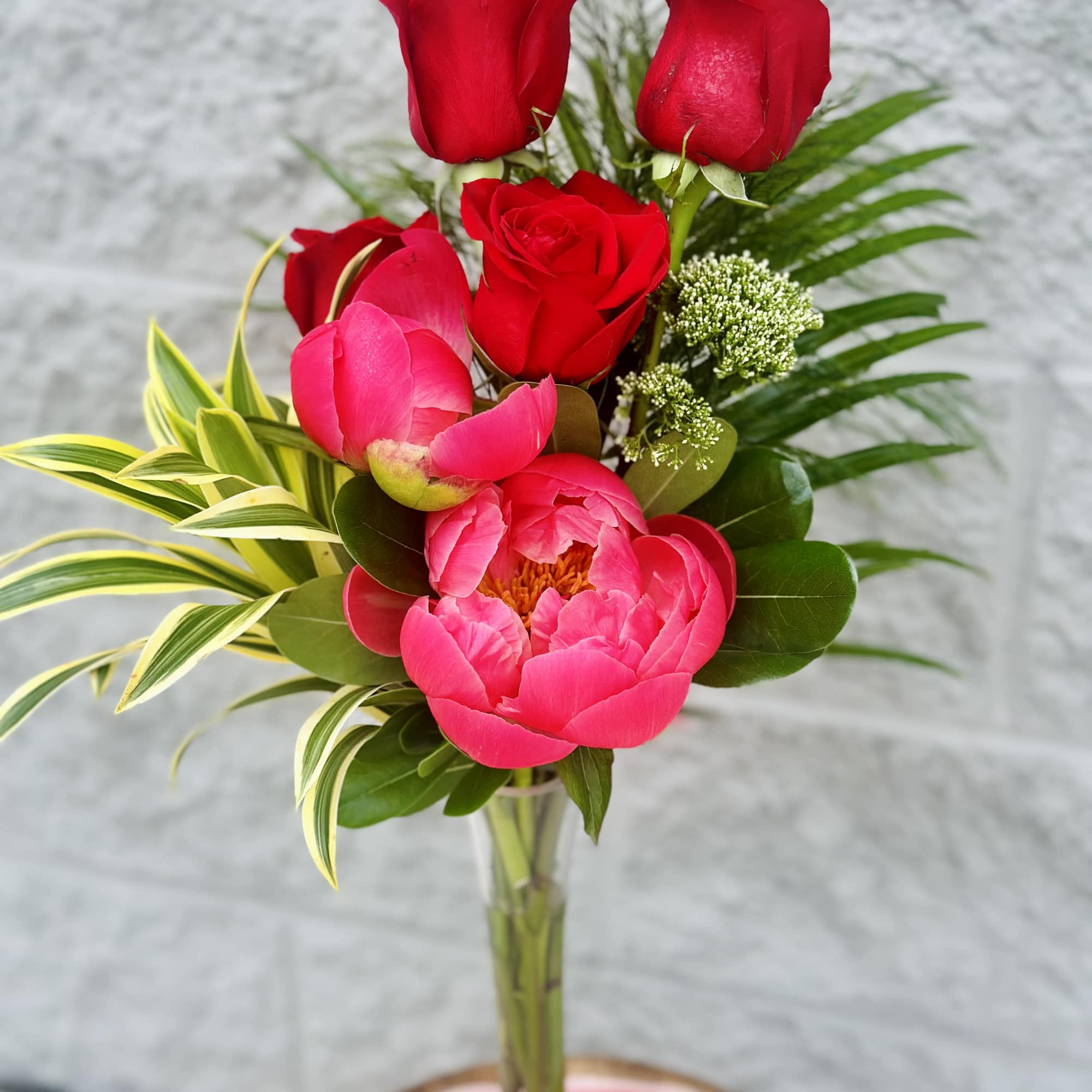 Red roses and a pink peony in a clear vase